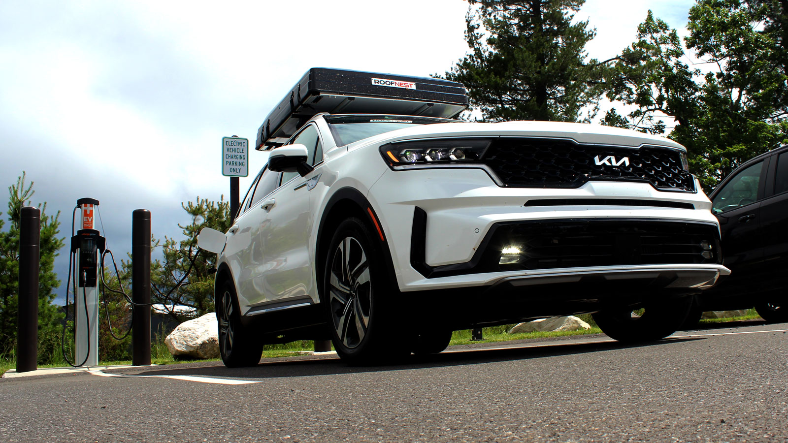 A photo of a white Kia Sorento SUV charging at a public plug. 