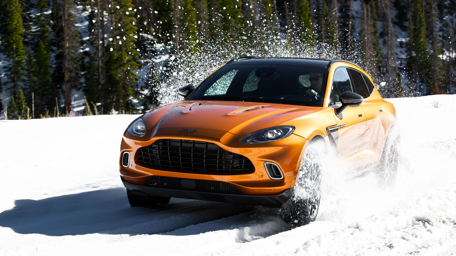 A photo of an Aston Martin DBX driving in snow. 