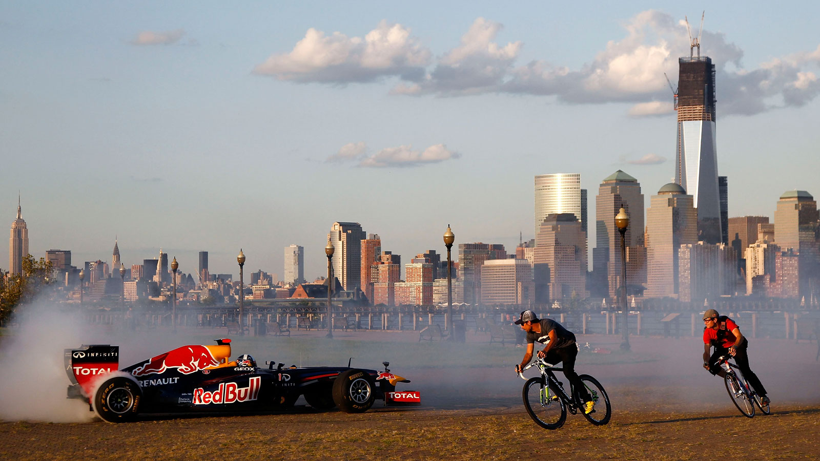 A photo of a Red Bull F1 car driving in New Jersey with the New York skyline in the background. 