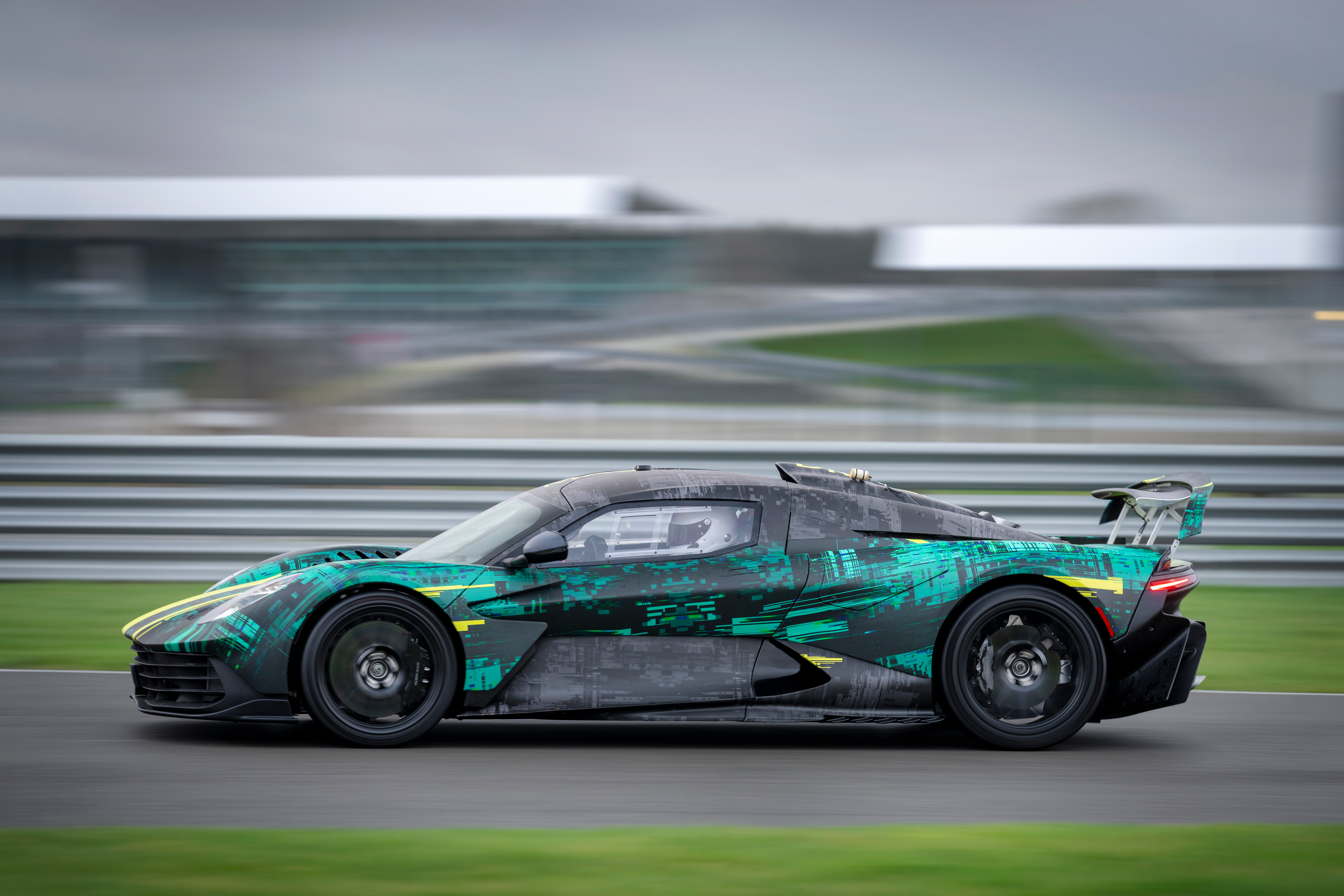 Side view of a camouflaged Aston Martin Valhalla driving on track