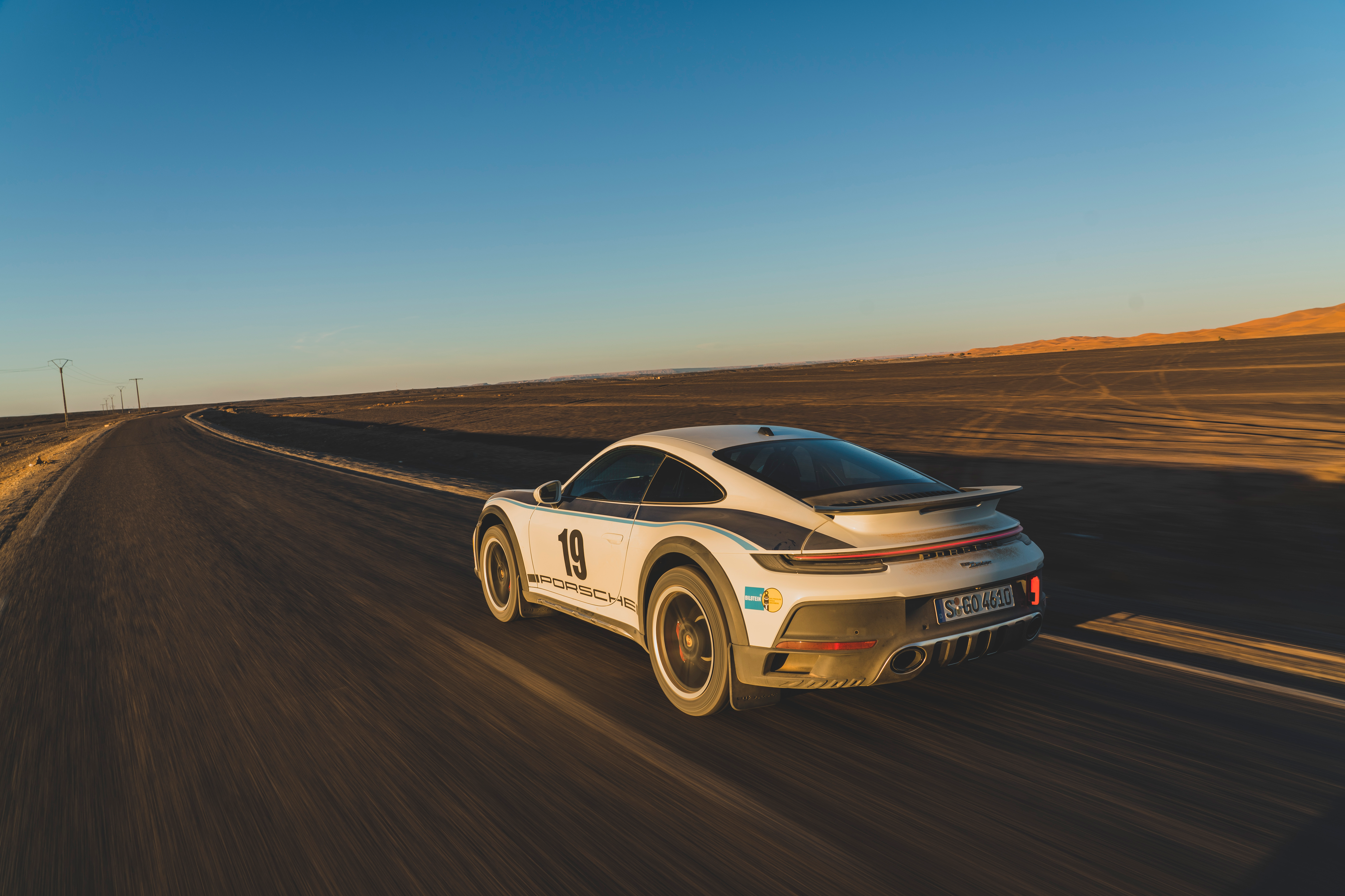 A Porsche 911 Dakar speeds down a desert road in a Rallye 1974 livery