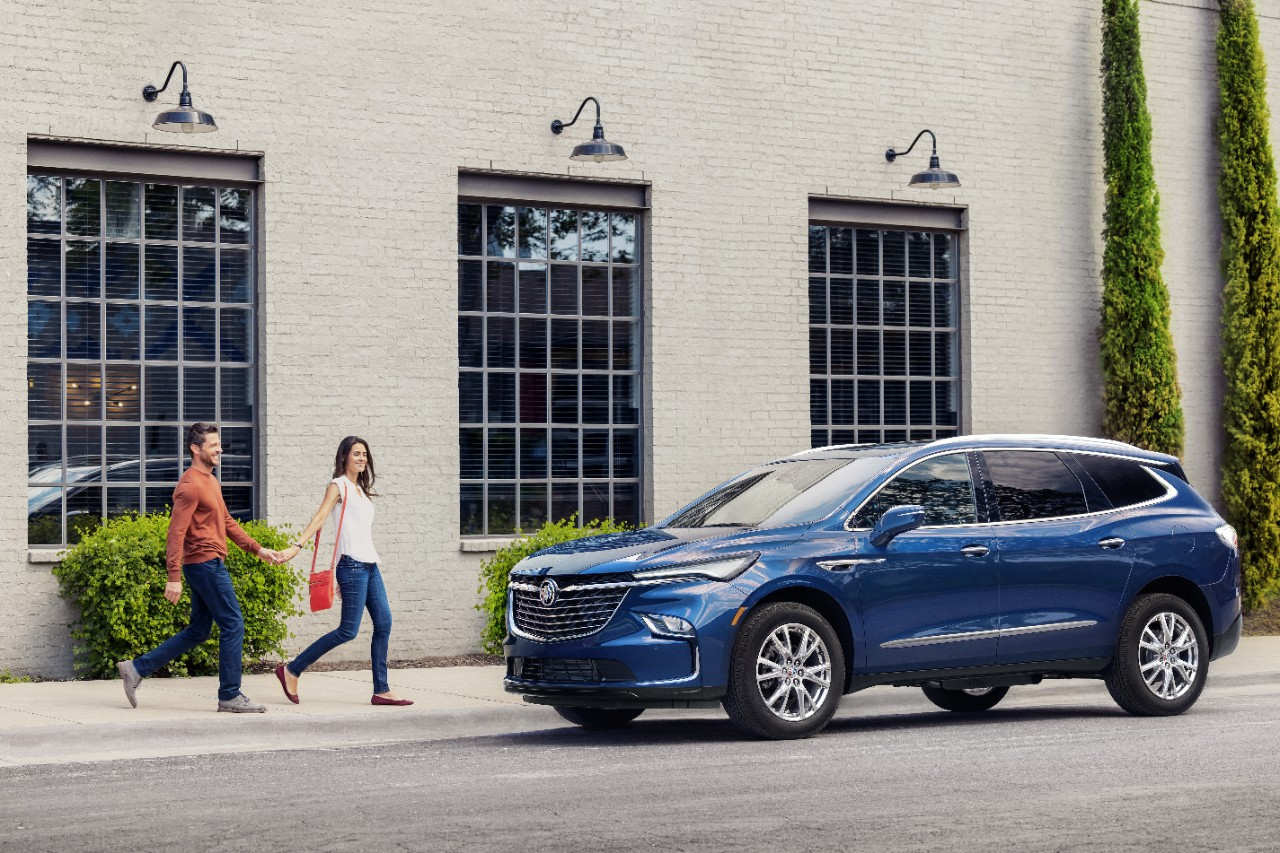 A blue Buick Enclave with a man and woman holding hands walking up to it.