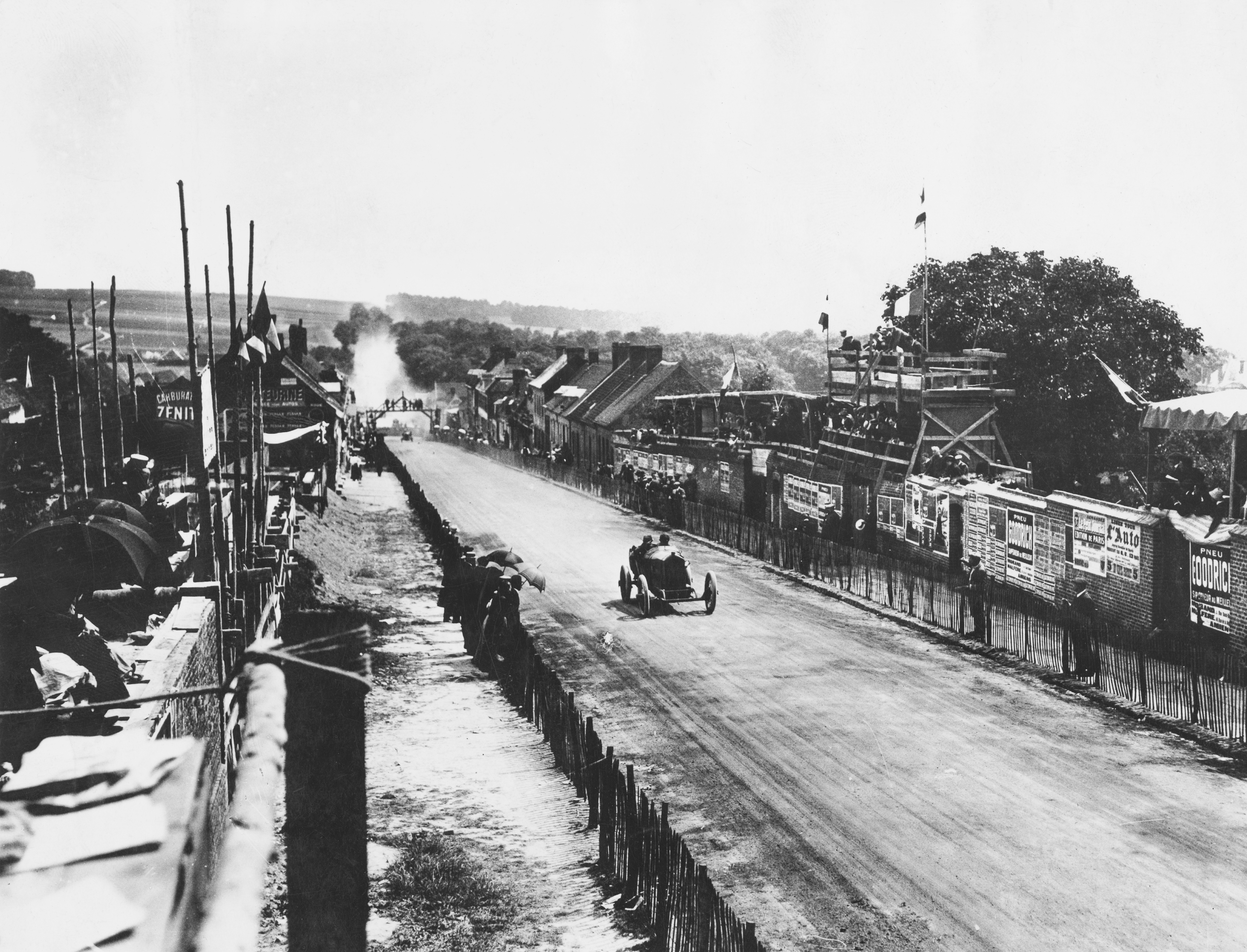 Spectators line the course as Jules Goux of France drives the #14 Peugeot EX3 through Moreuil during the Grand Prix de l'Automobile Club de France on 12 July 1913 at the Amiens circuit, France