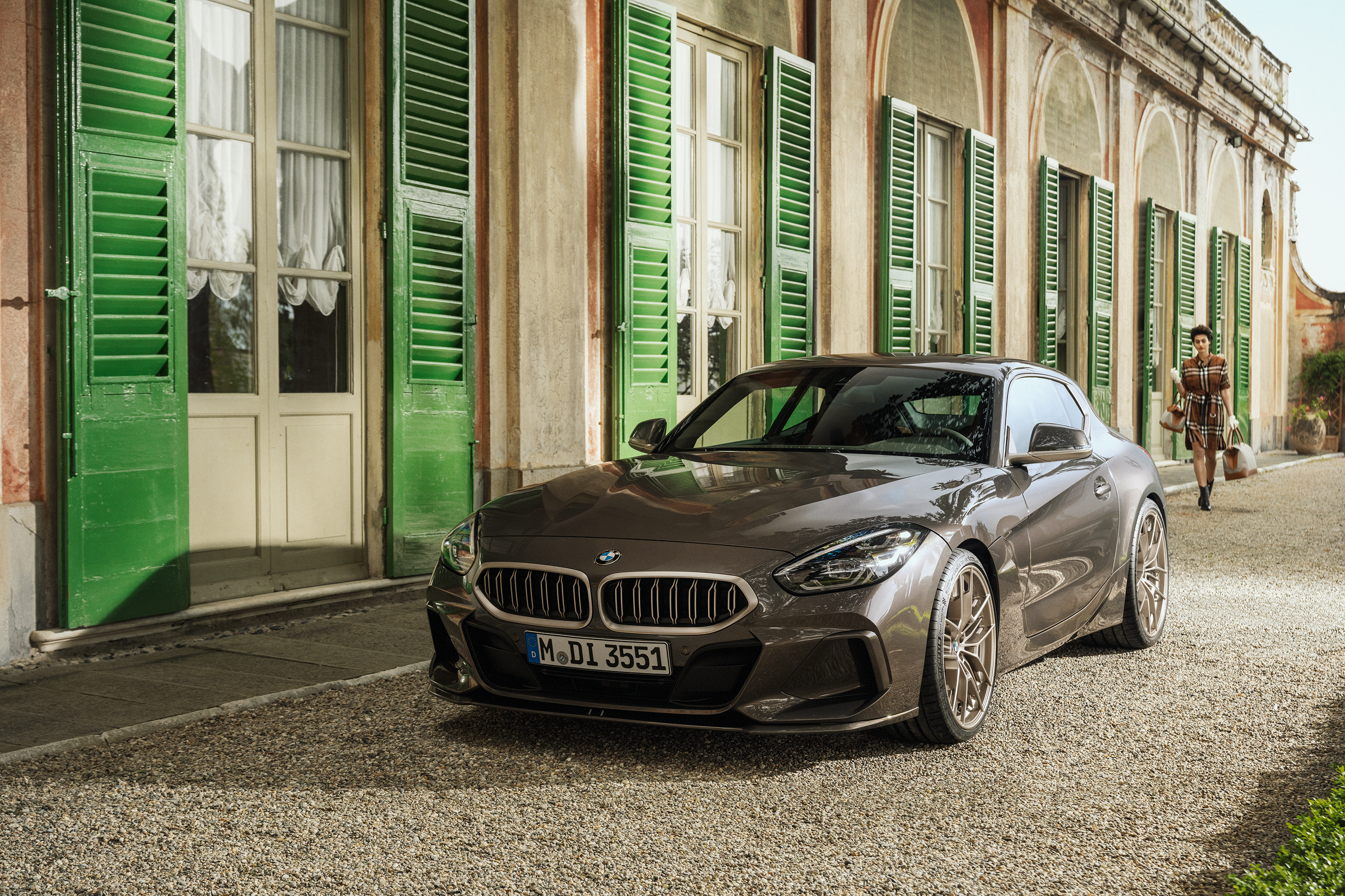 A brownish gray BMW shooting brake concept car is parked in front of a building with green shutters. Front three quarters view.