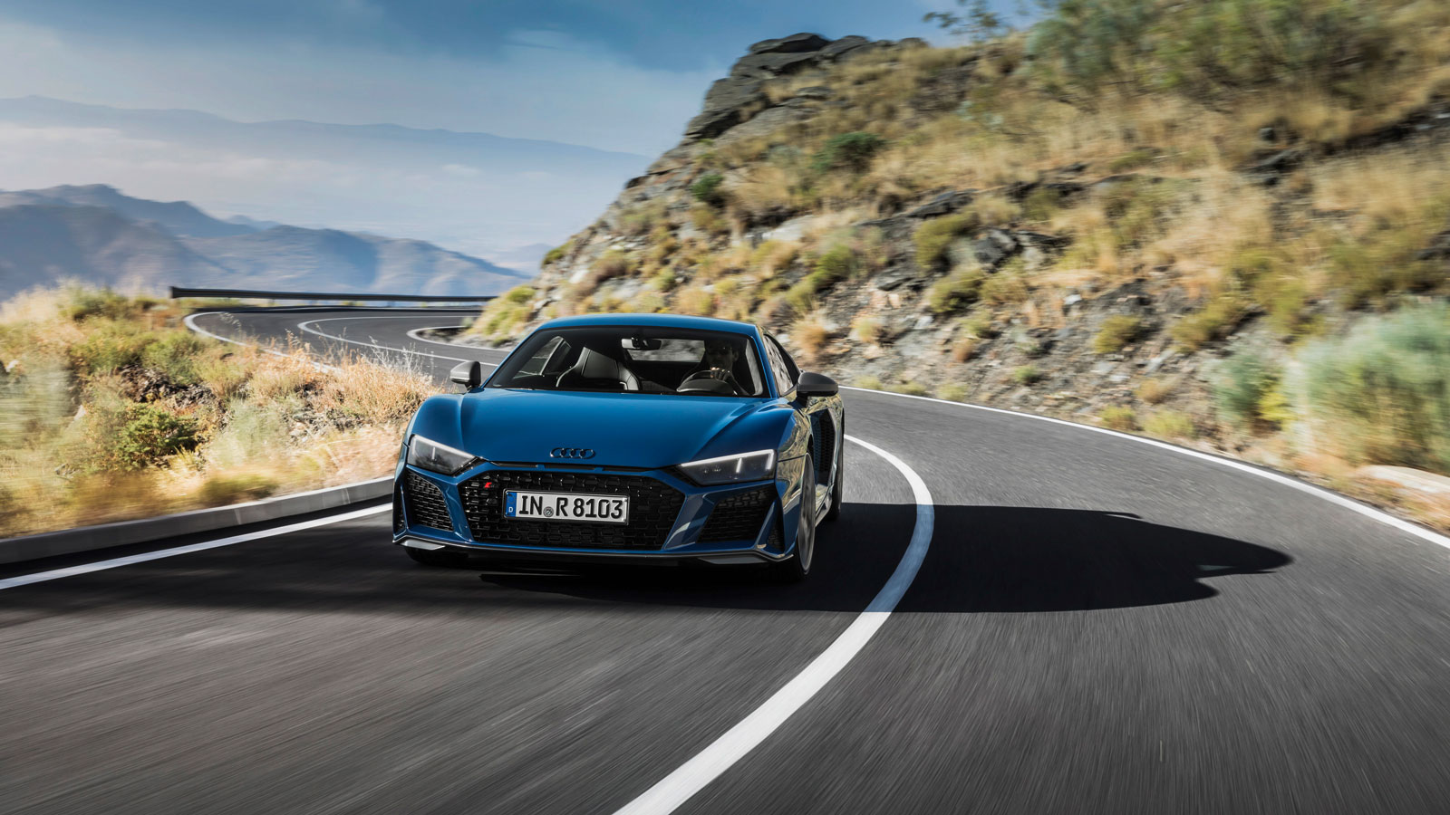 A photo of an Audi R8 supercar driving on mountain roads. 