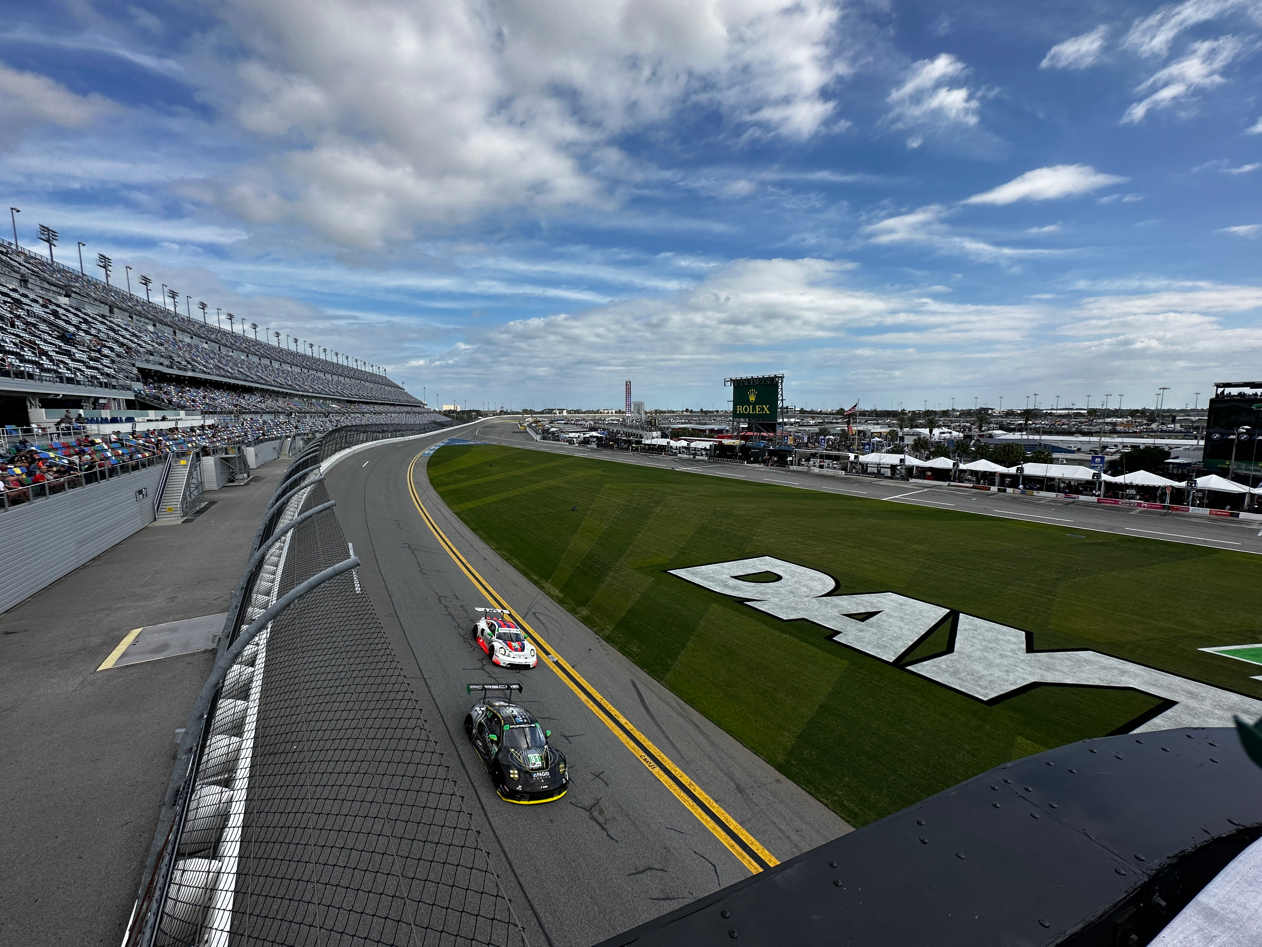 Two racing Porsche 911s drive by the starting stand at Daytona Speedway.