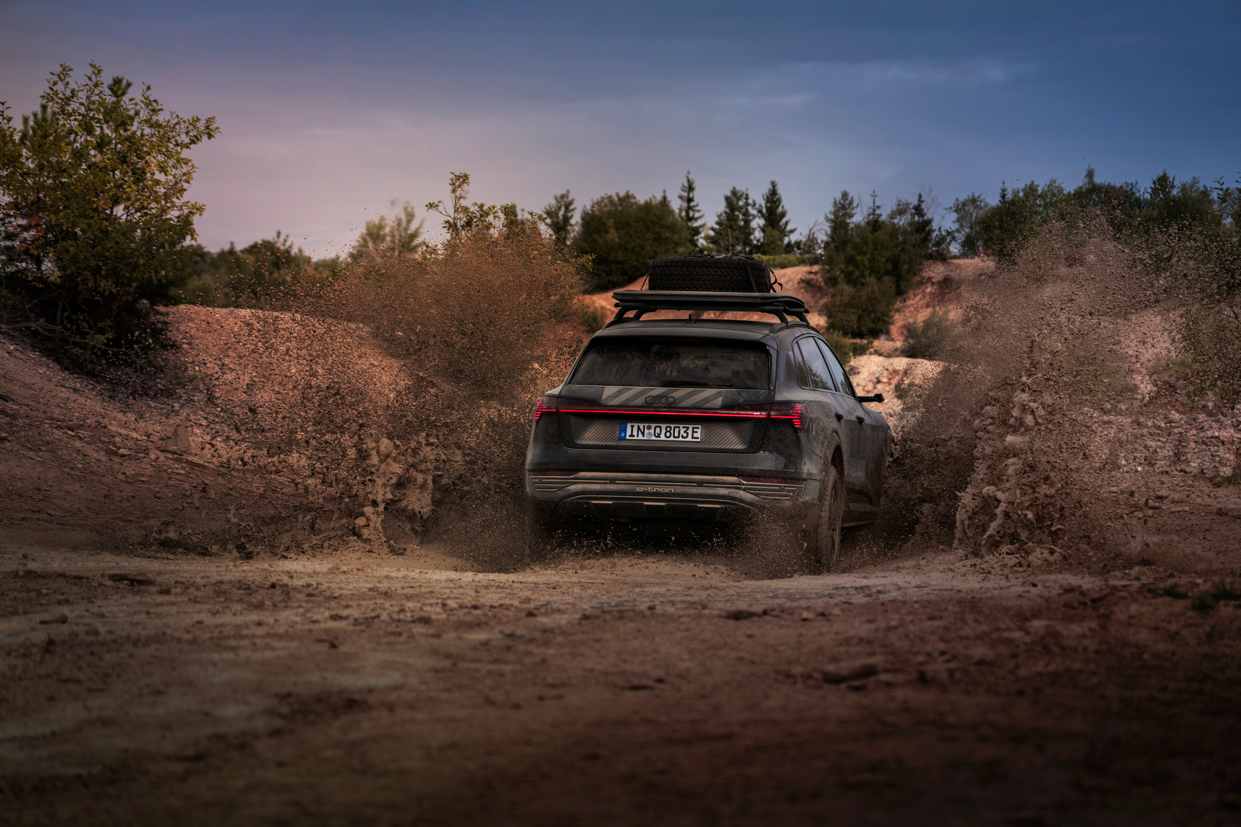 Rear 3/4 view of a black Audi Q8 E-Tron driving through mud