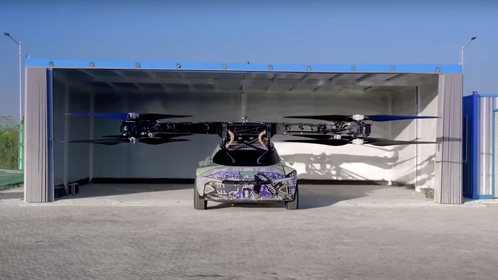 A photo of a flying car rolling out a large garage at an airfield. 