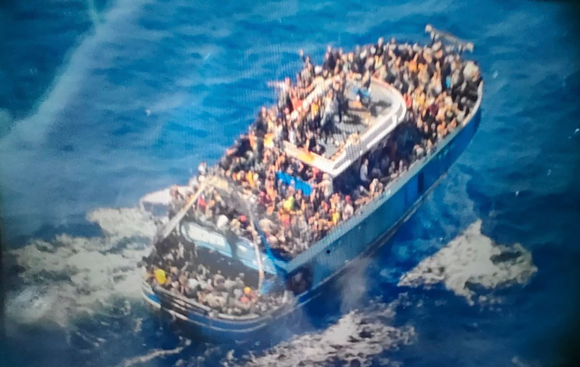 An image provided by the Greek Coast Guard showing a crowded blue fishing boat. Many people are visible aboard