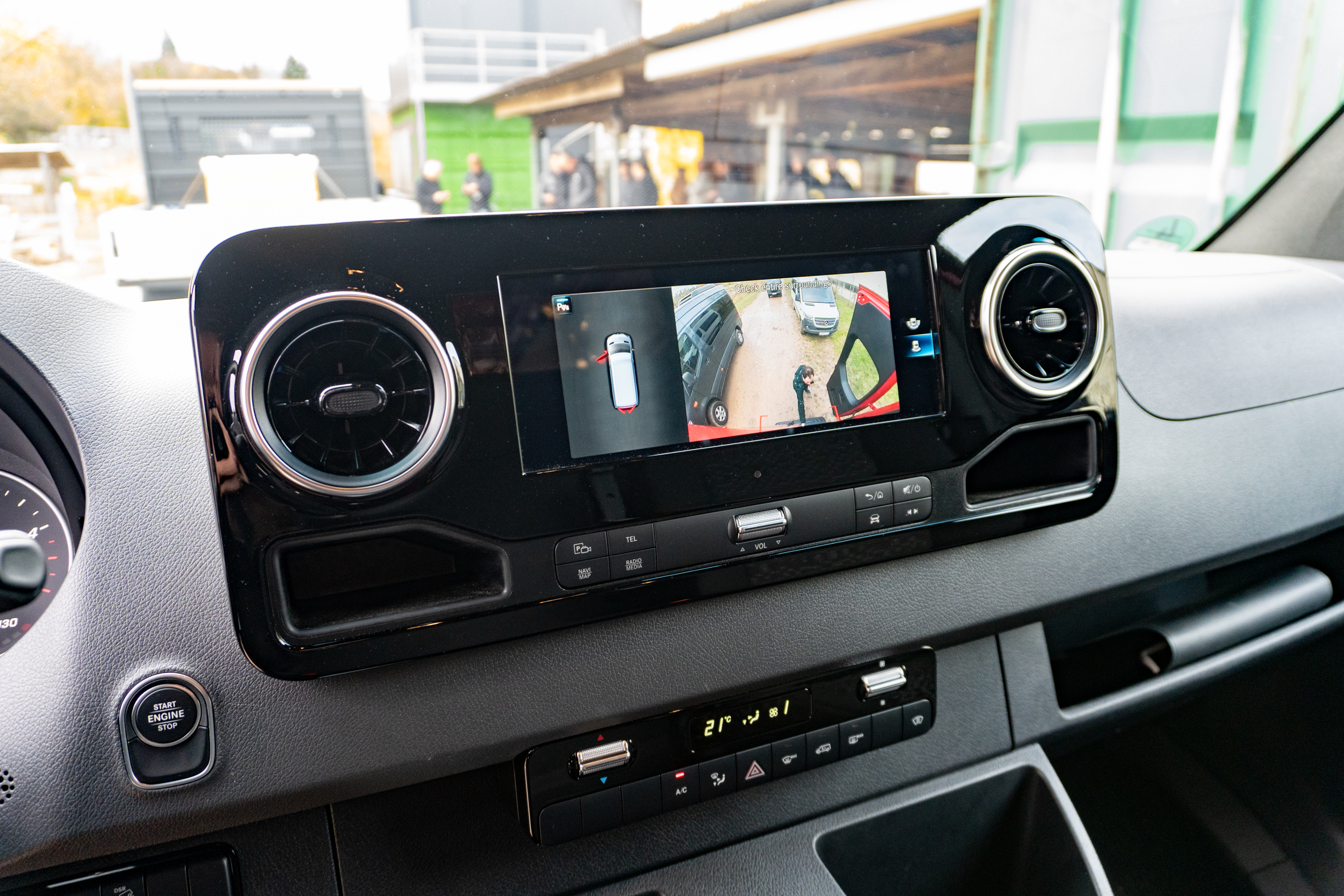 another view of the dashboard of the 2023 mercedes benz sprinter awd van. the screen in the center of the dash shows a view from the camera on the rear of the vehicle, letting the driver see the person loading cargo in the back of the van.