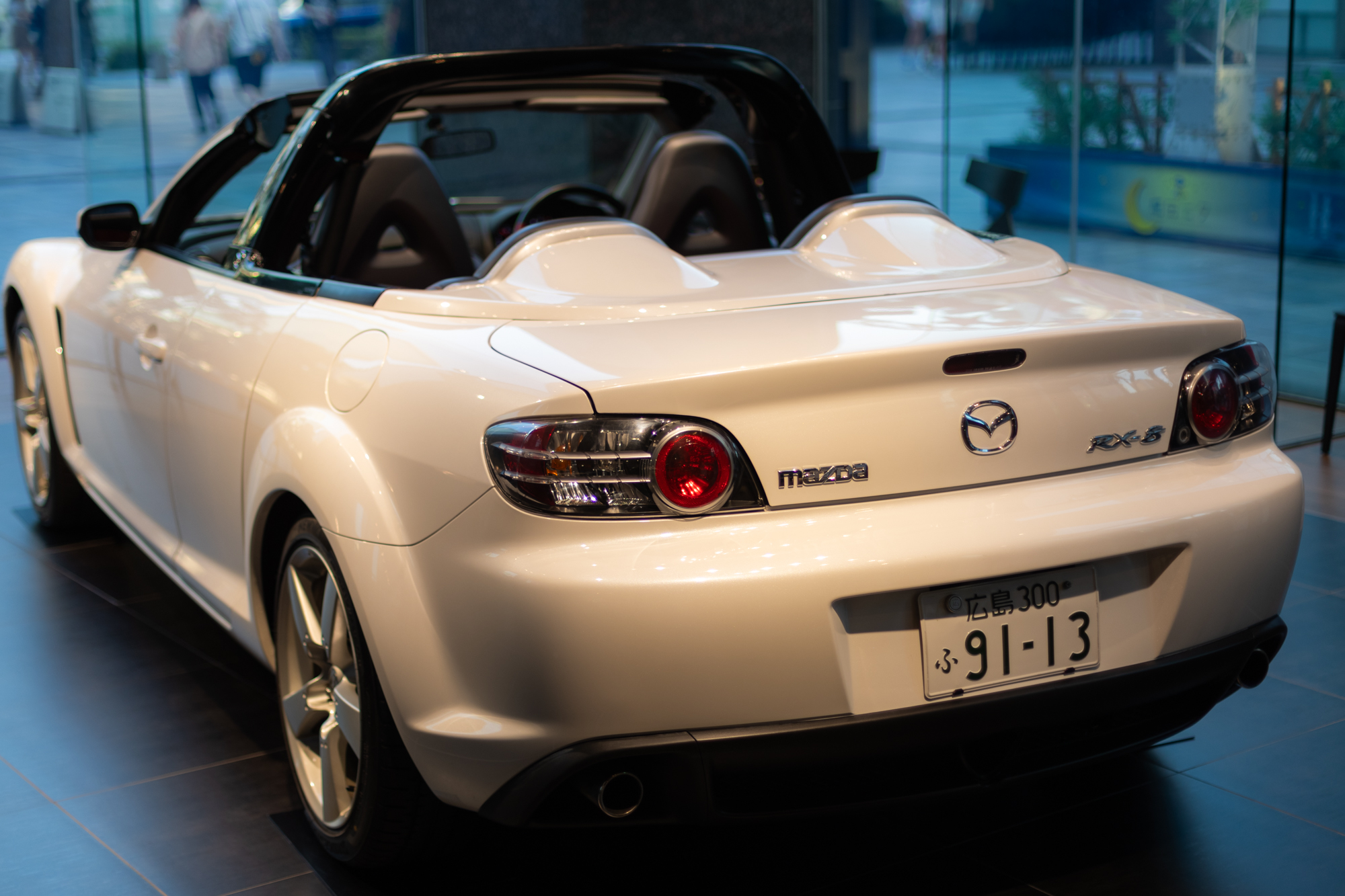 An image of the back of a white, roof-less Mazda RX-8 in one of the brand's showrooms.