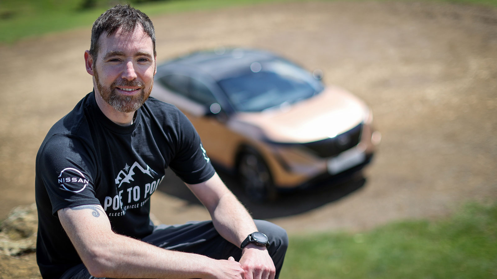 A photo of adventurer Chris Ramsay with a Nissan EV in the background. 