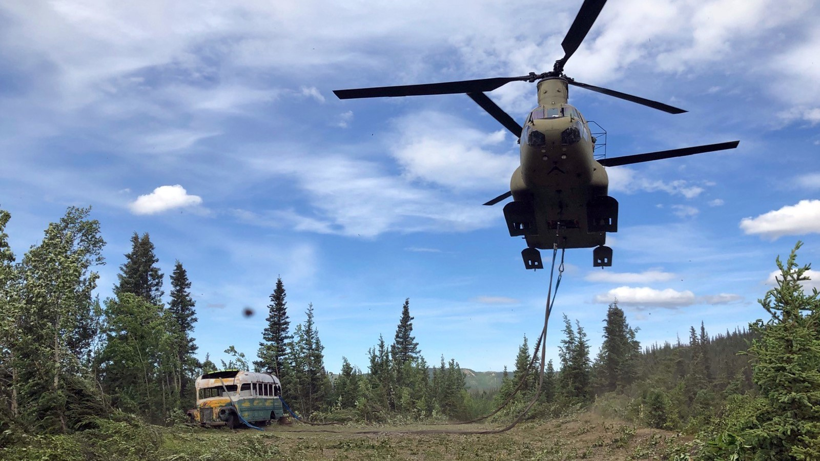 A chinook helicopter takes off with a bus attached below. 