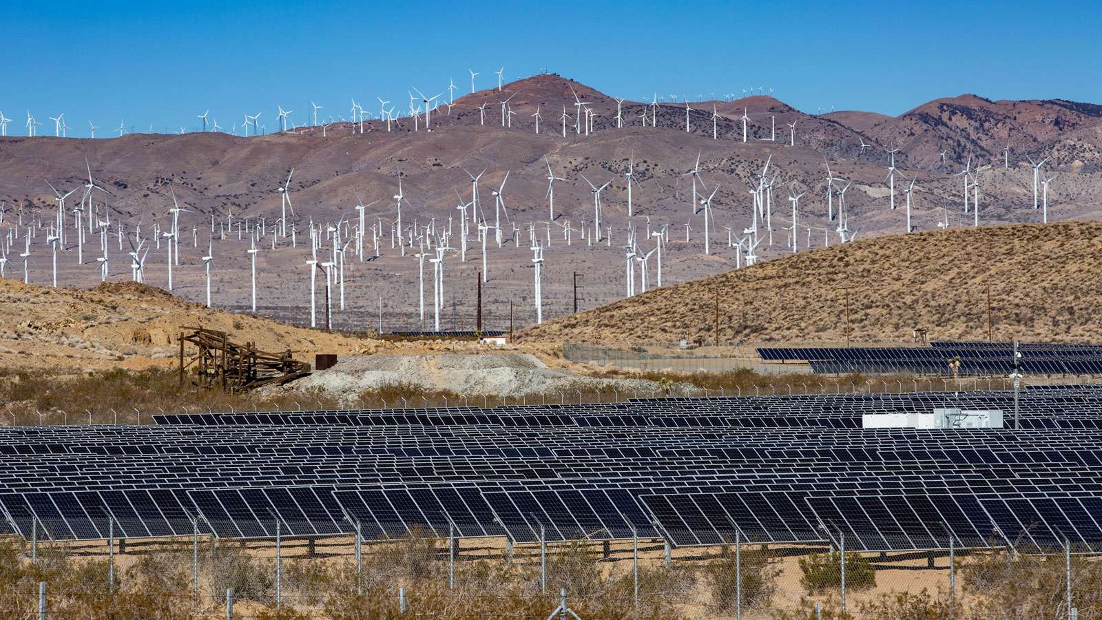 A photo of solar panels with a wind farm in the background. 