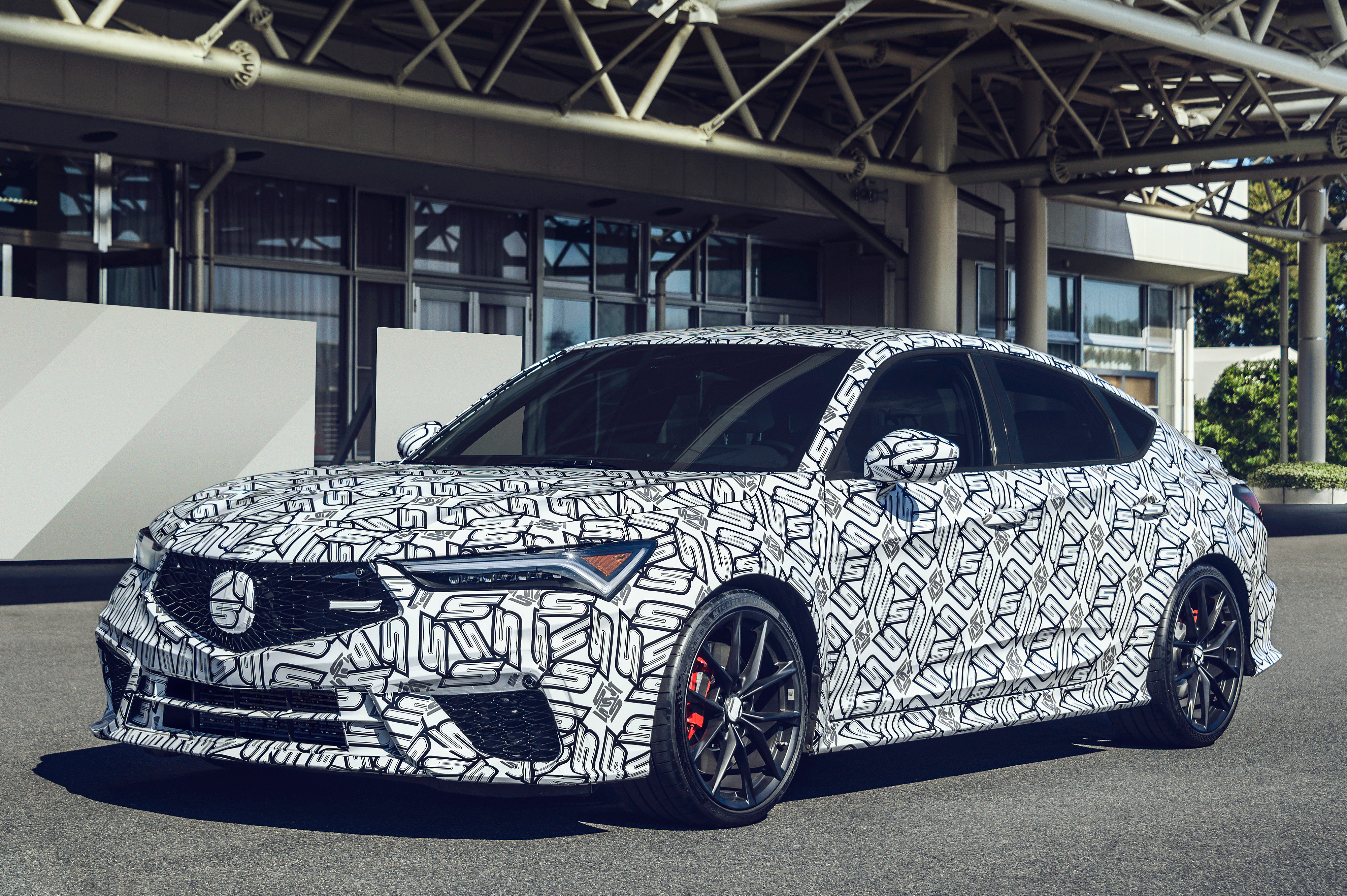 a 2024 acura integra type s prototype seen from a front-left 3/4 view parked in an industrial setting. the car is wrapped in black and white camouflage