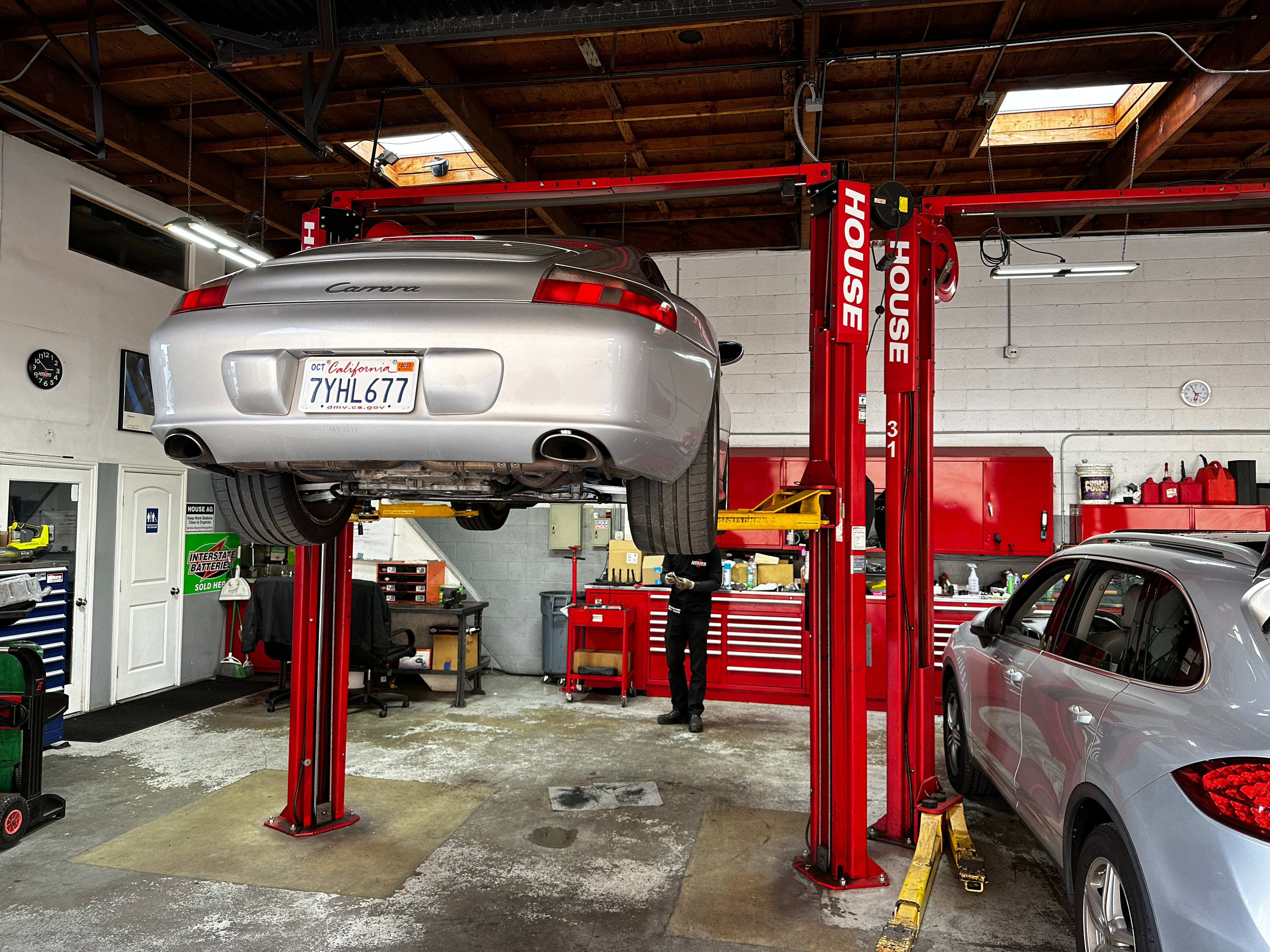 A silver 2003 Porsche 911 is on a lift being repaired.