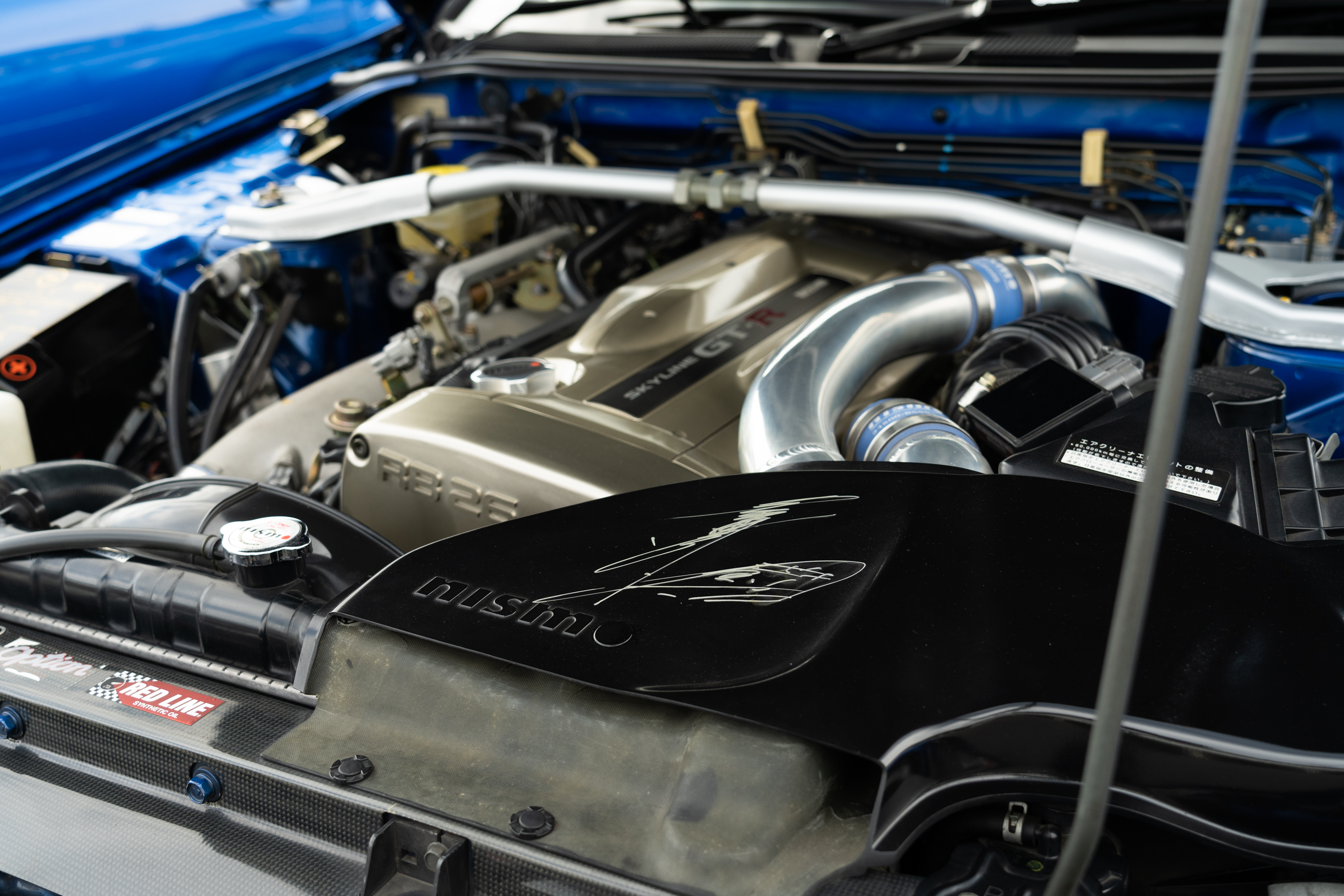 a close-up shot of the engine of an R34 nissan gt-r, with engineer hiroshi tamura's signature on the air intake