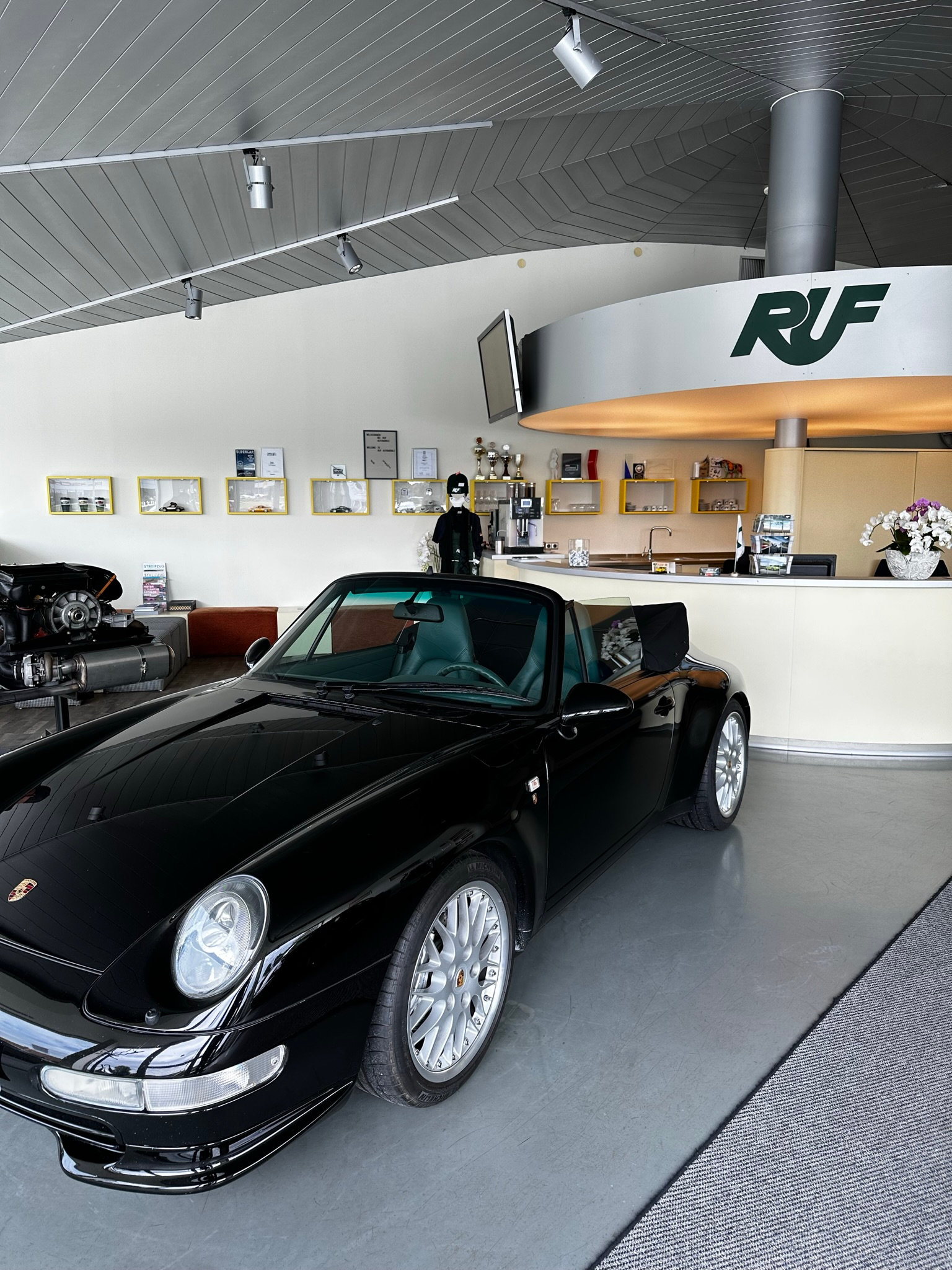 The showroom and lobby of Ruf Automobile in Pfaffenhausen, Germany. There is a black 993-generation 911 cabriolet parked inside.