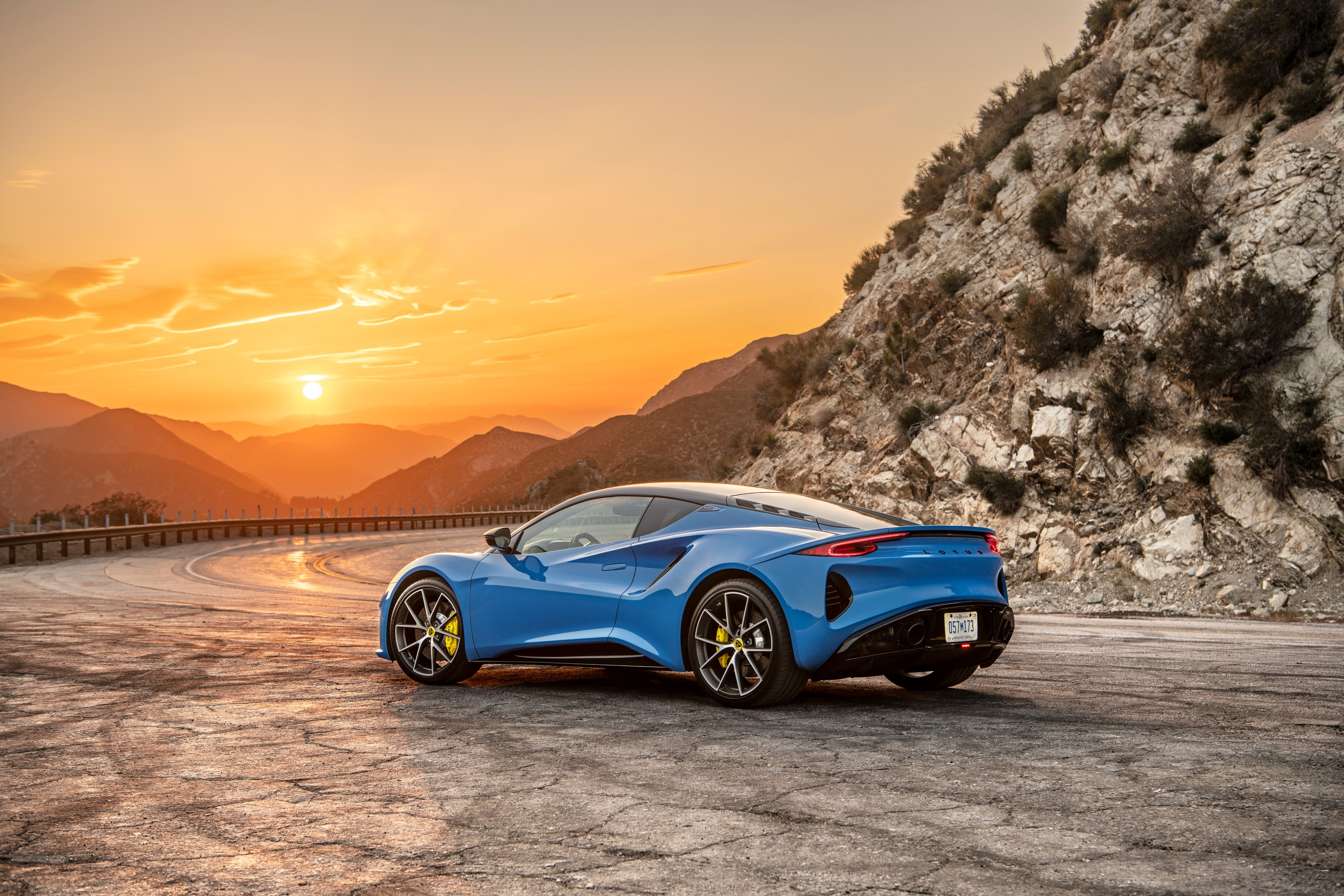 The 2023 Lotus Emira in Seneca Blue, rear three quarter view in front of a rocky cliff.