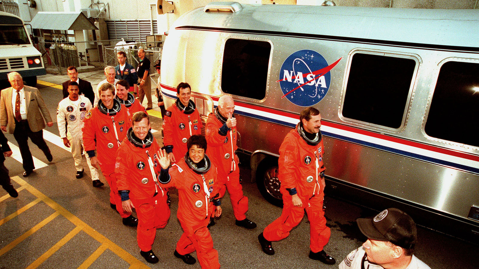 A photo of space shuttle astronauts walking past their transport vehicle. 