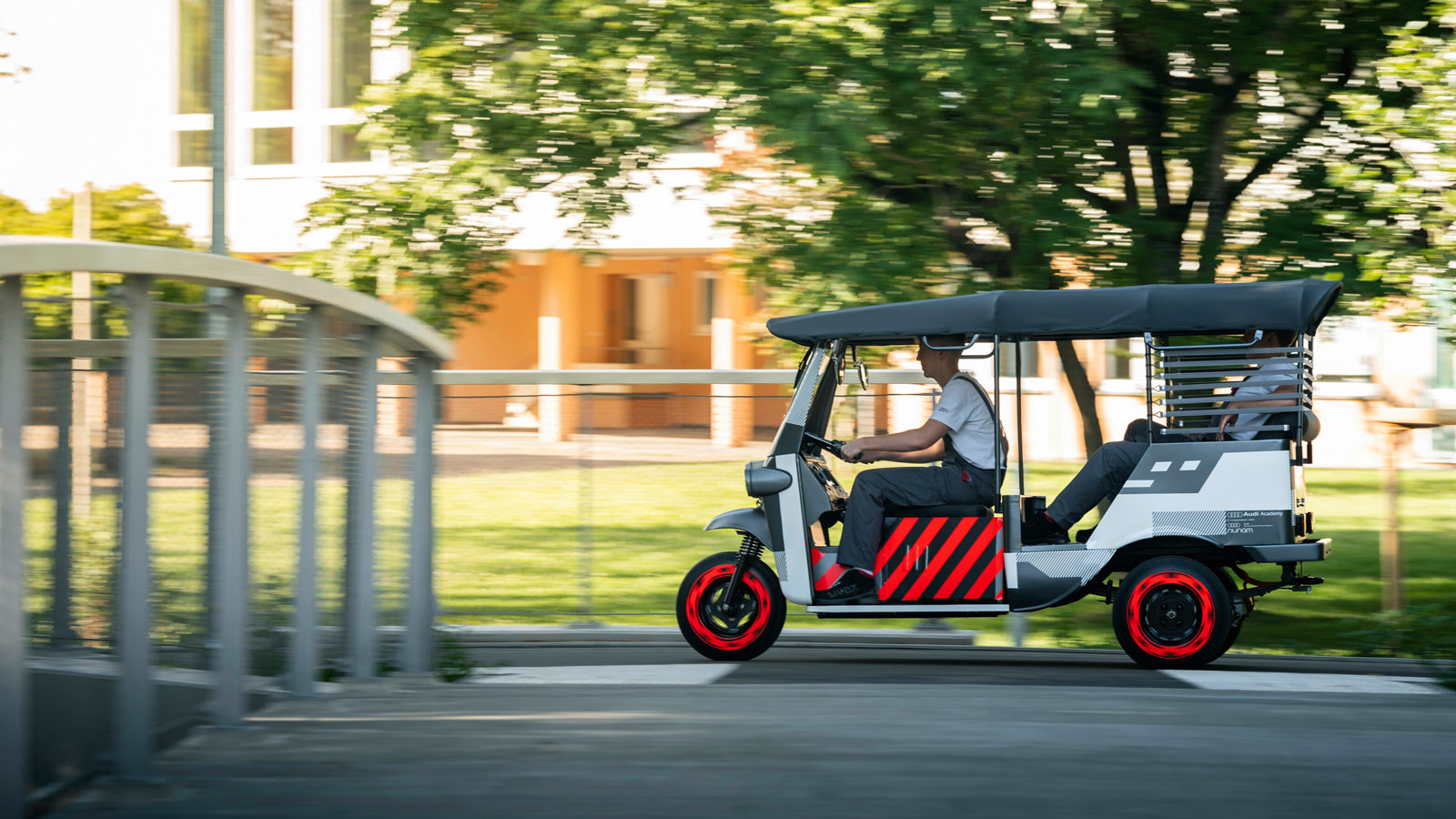 A side profile view of a battery-powered rickshaw as it drives through a park. 