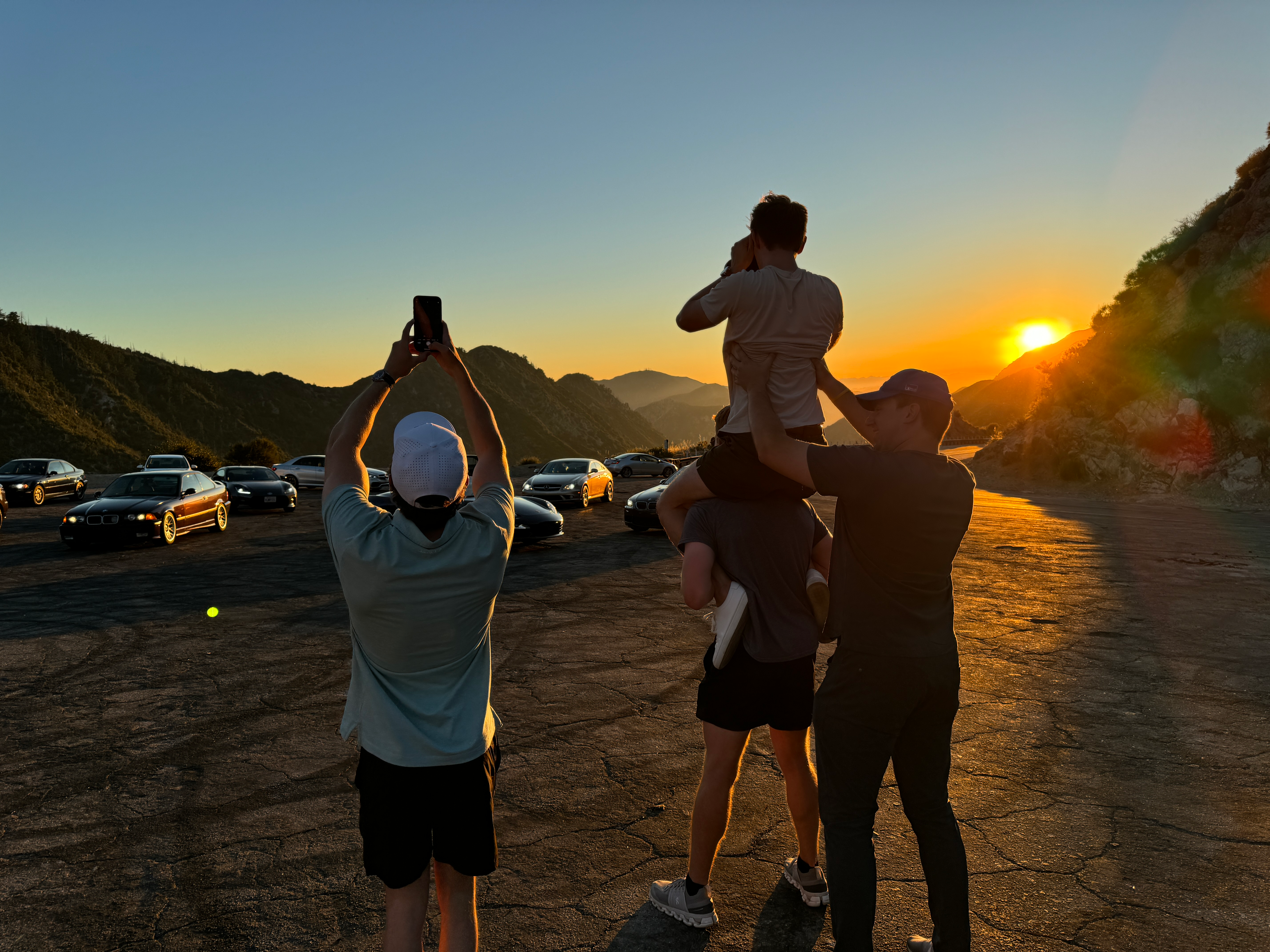 Four guys taking photos of a group of cars at sunset