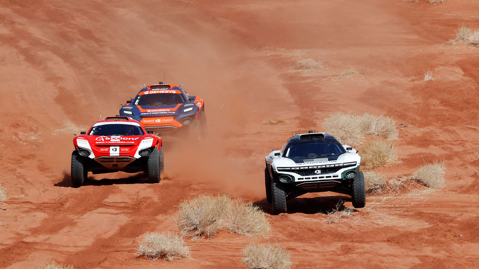 A photo of three Extreme E cars racing on sand. 