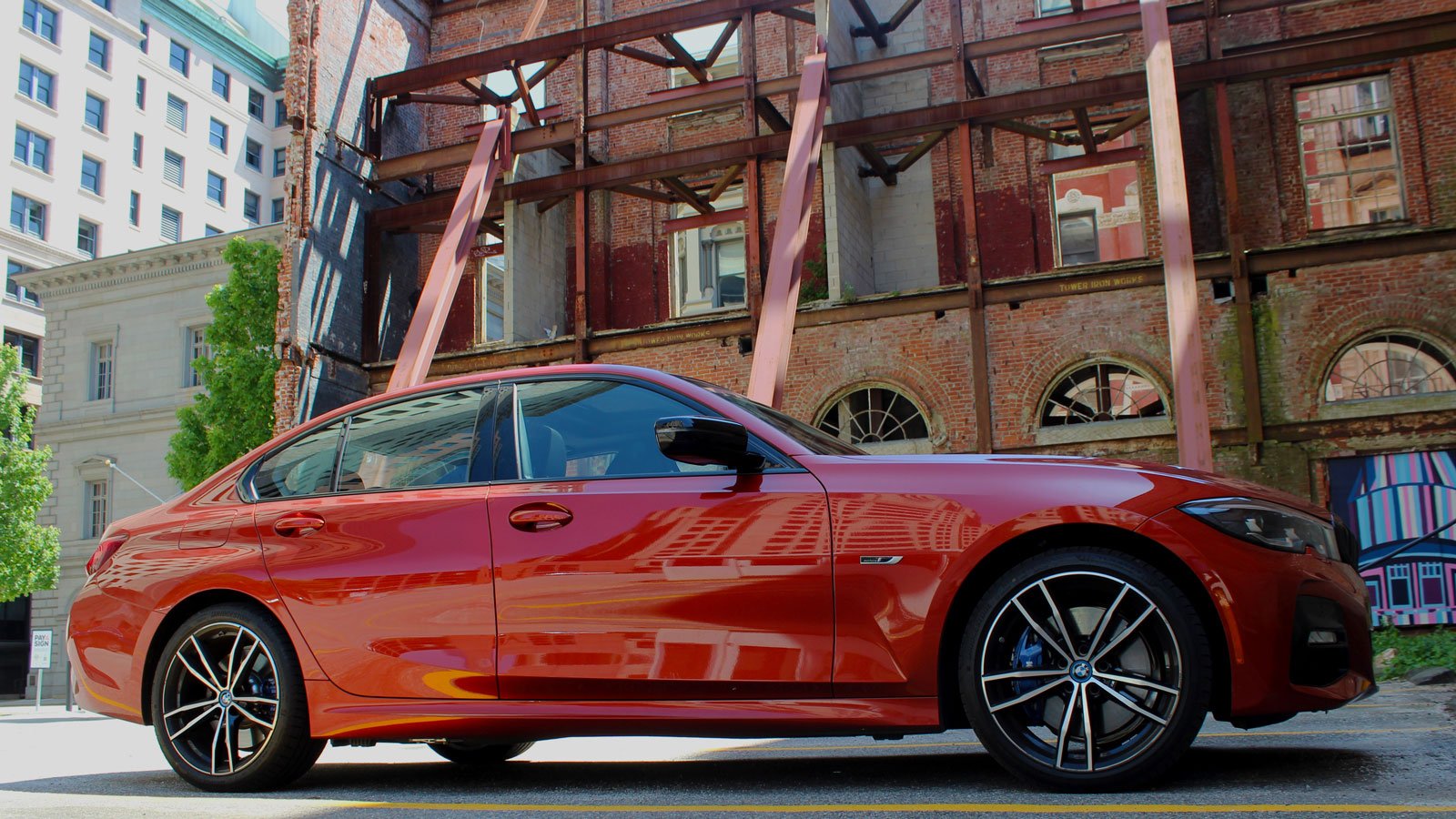 A side photo of the BMW 330e sedan parked behind the shell of an old building. 