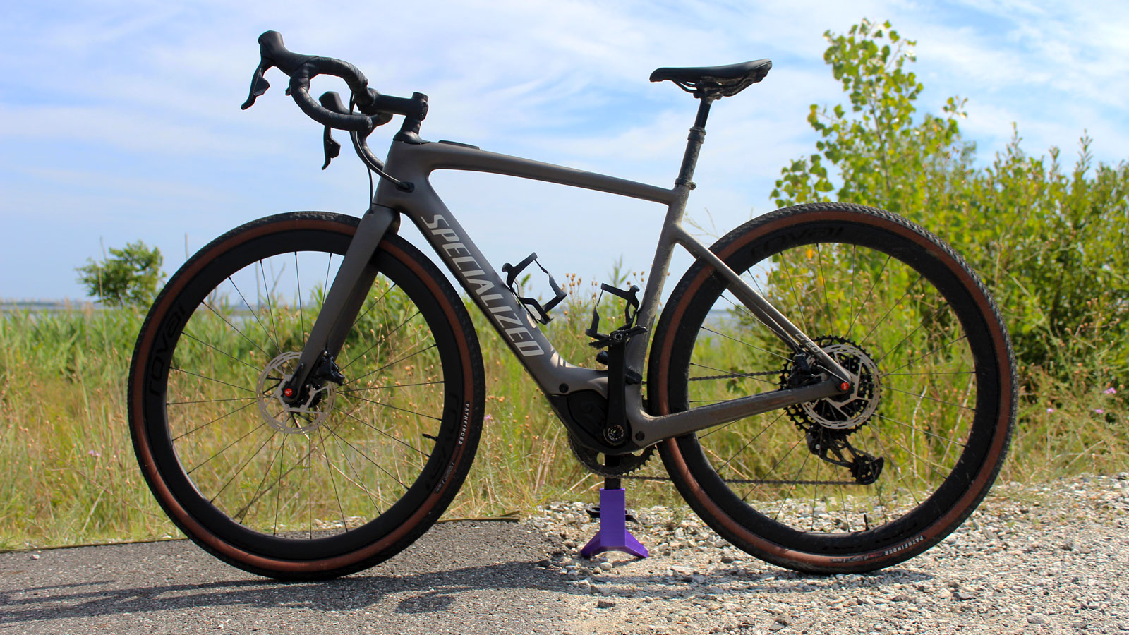 A photo of a Specialized Creo SL electric bike half on a dirt track and half on paving. 