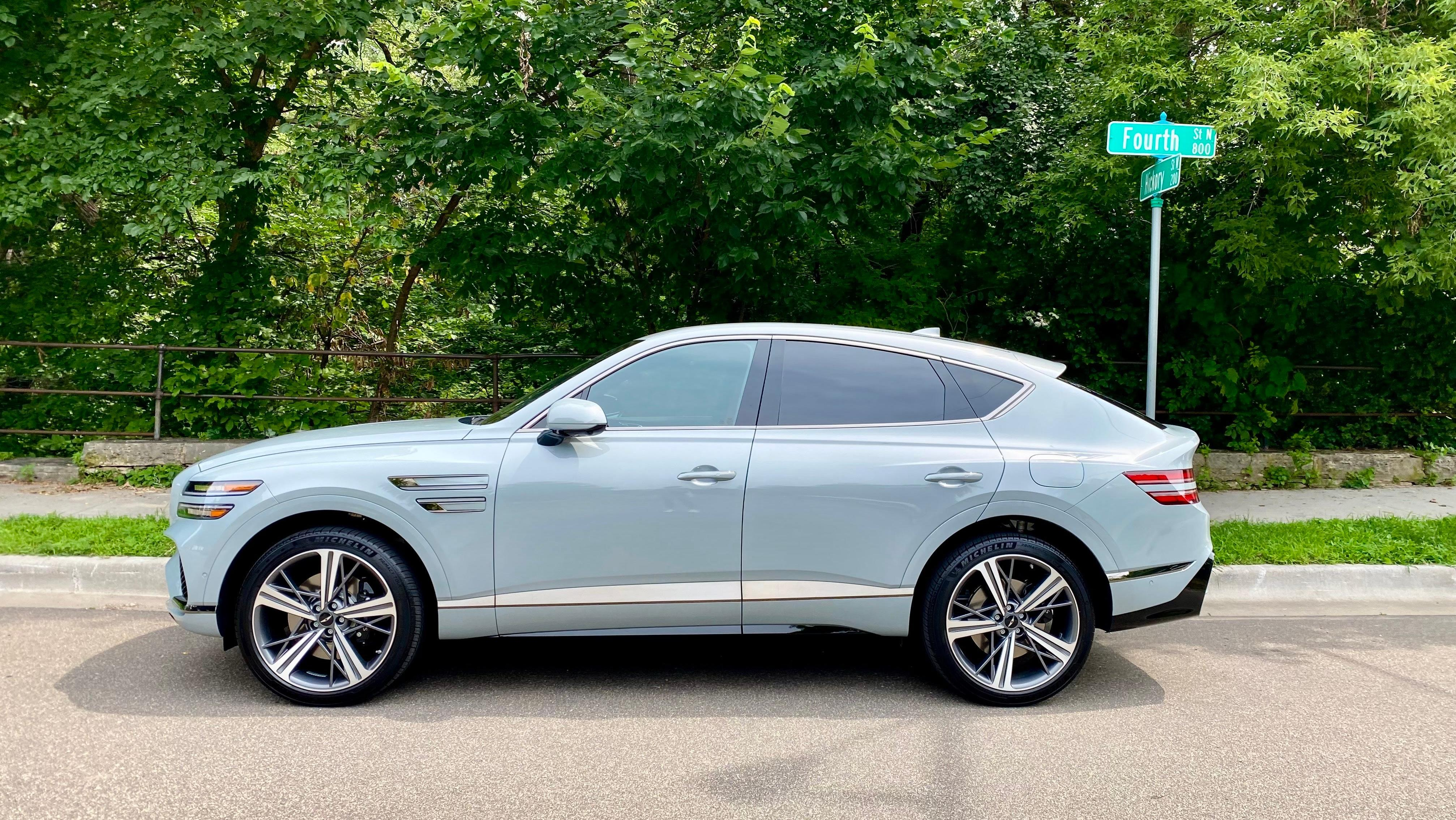 A side view of a Bering Blue GV80 Coupe parked in front of trees