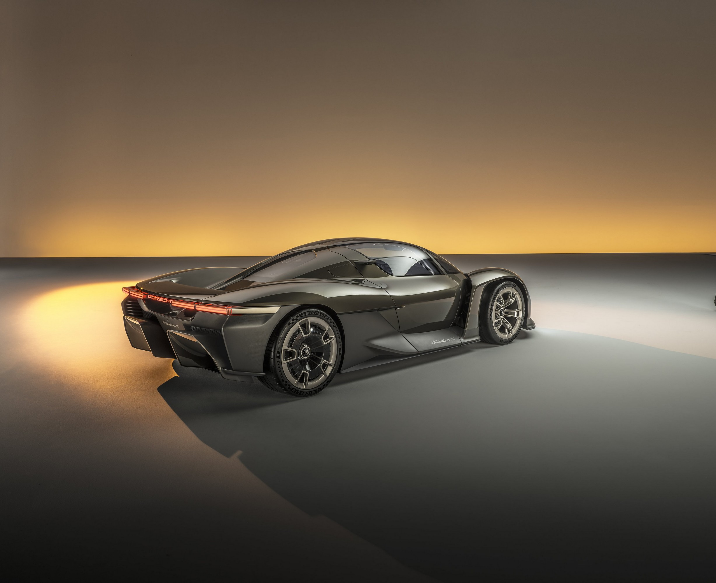 The Porsche Mission X electric hypercar concept is parked in a studio. Rear-three-quarter view.