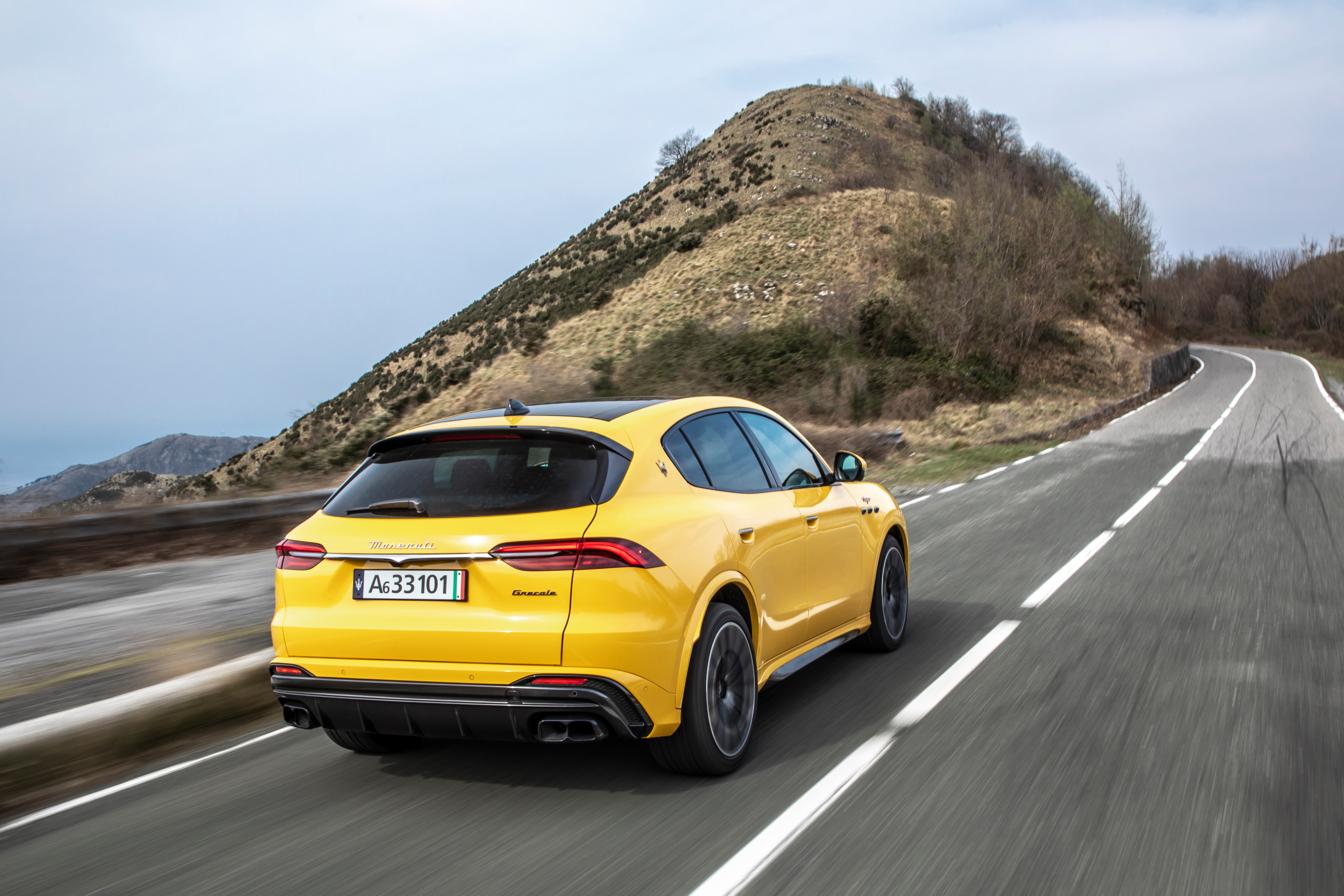 The yellow 2023 Maserati Grecale Trofeo drives along a mountain road, rear three-quarter view