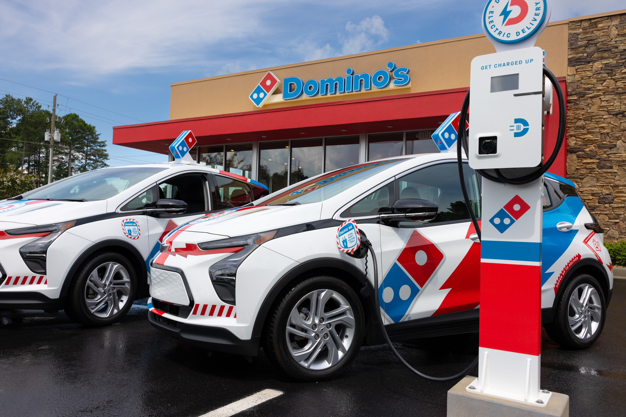 A Domino's liveried Bolts charging at a station in front of a company location.