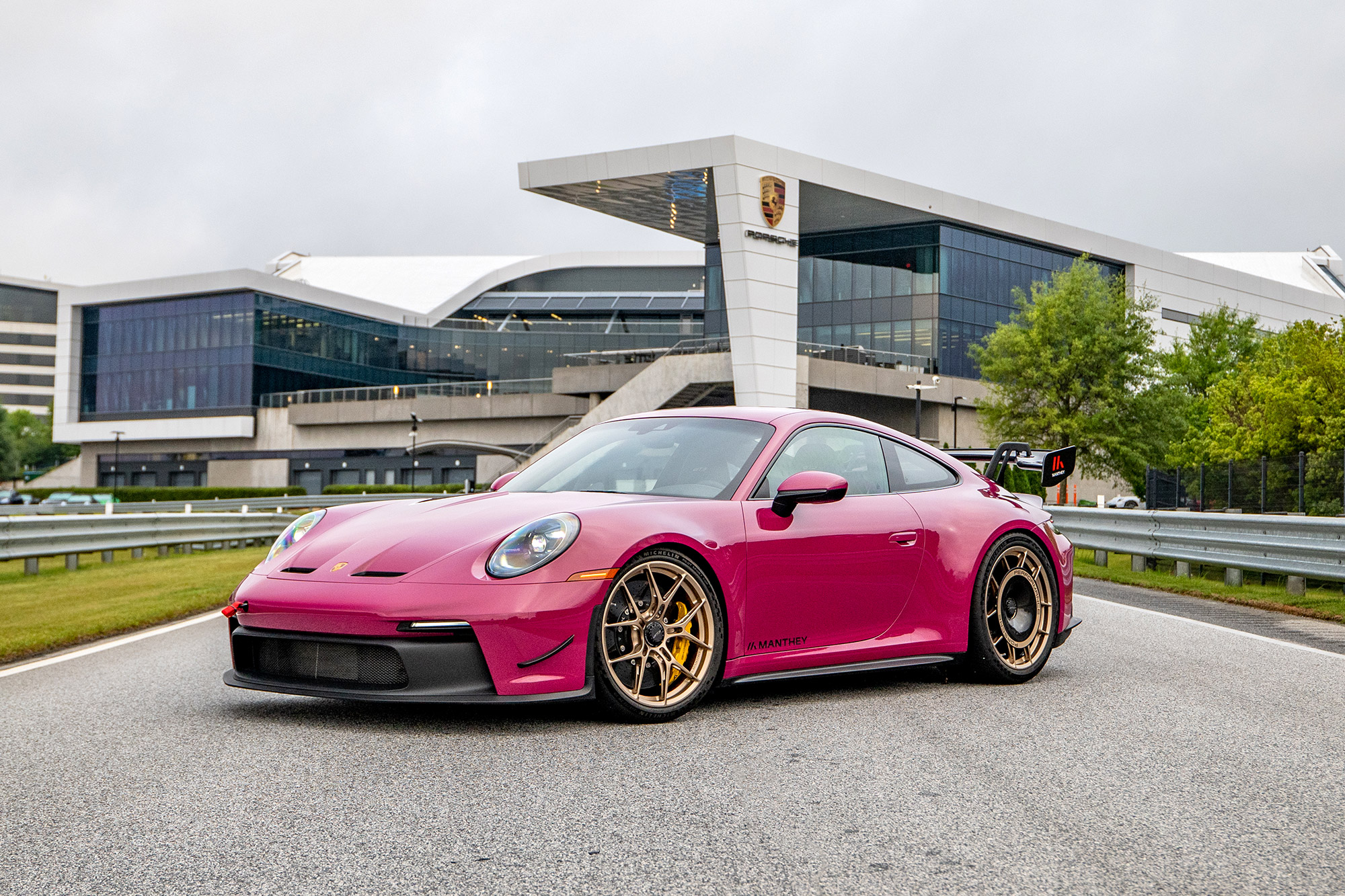 A ruby Porsche 911 GT3 equipped with the Manthey Performance Kit parked in front of Porsche headquarters, viewed from the front quarter.