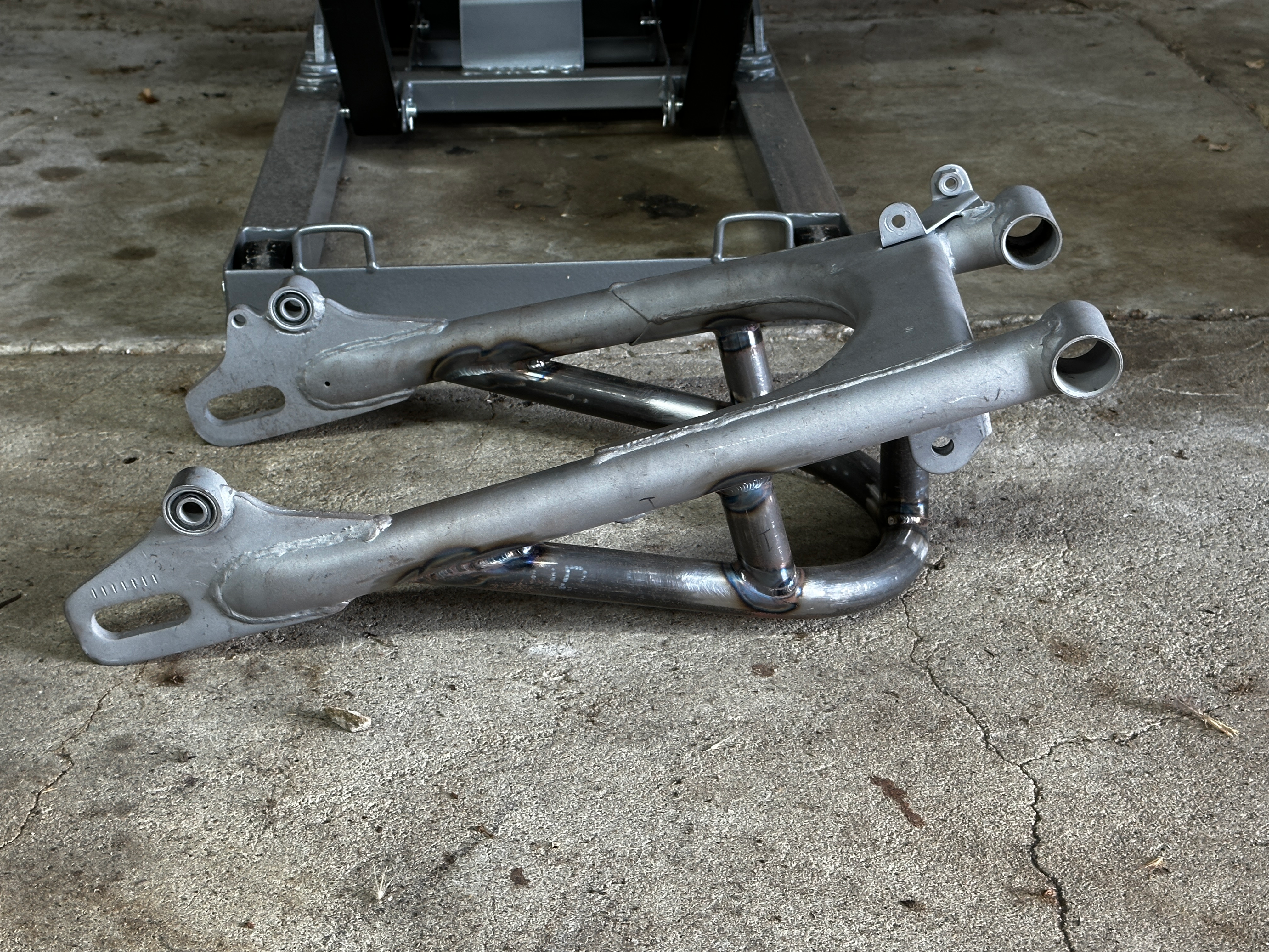 A modified Honda CB350 rear swingarm sits on concrete.