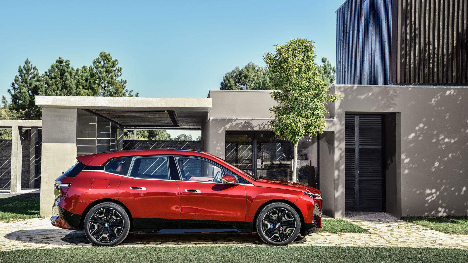 A photo of a red BMW iX SUV parked outside a house. 