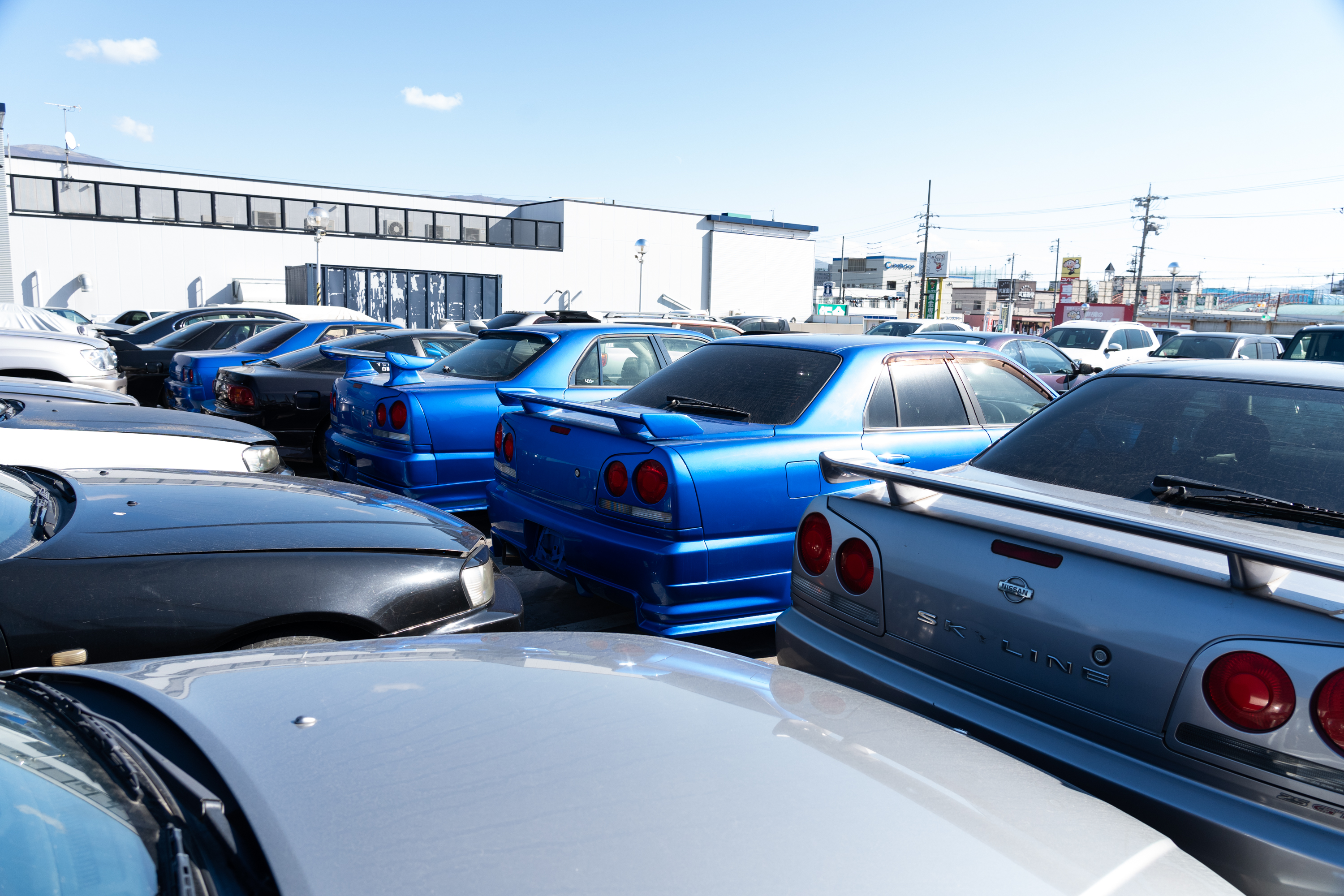 three r34-generation nissan skylines seen from the rear, parked in a densely packed outdoor storage lot in japan