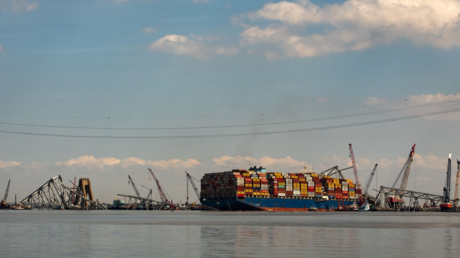 A photo of a container ship under the wreckage of a bridge. 