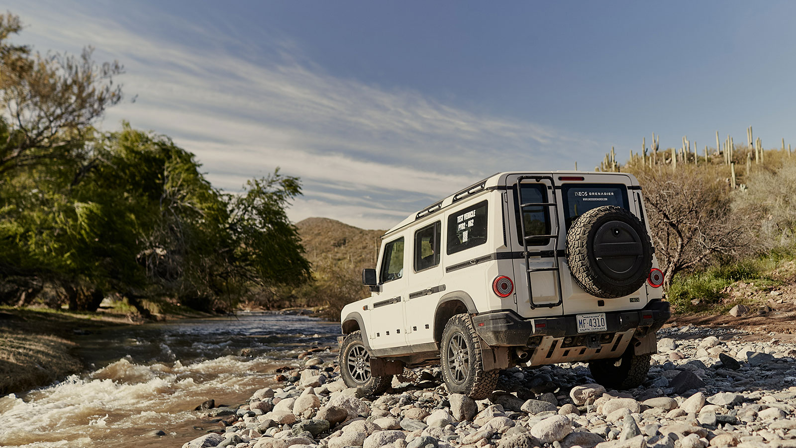 A photo of the Ineos Grenadier SUV parked near a river. 