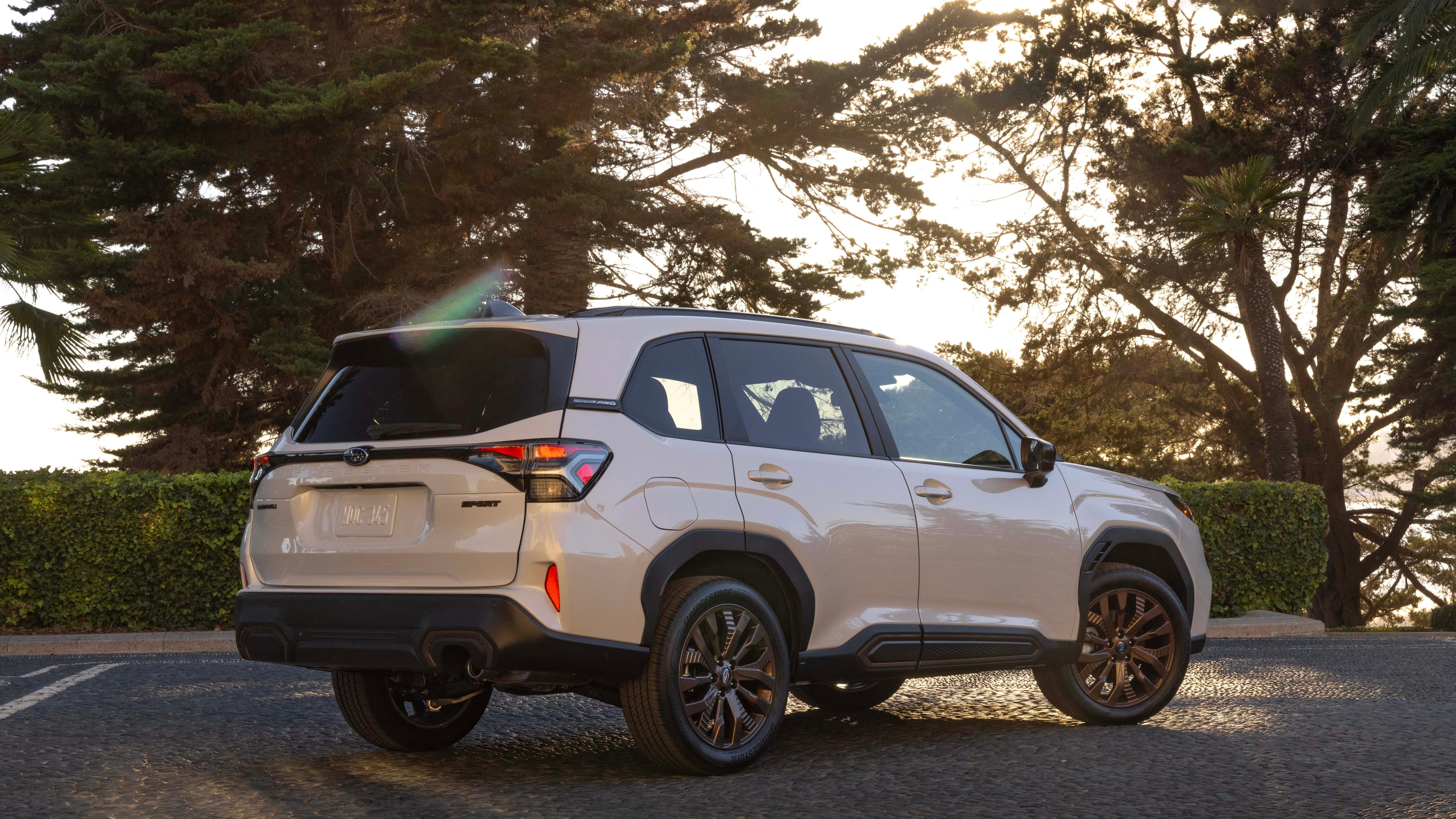 A white 2025 Forester from the rear 3/4 angle parked in front of trees