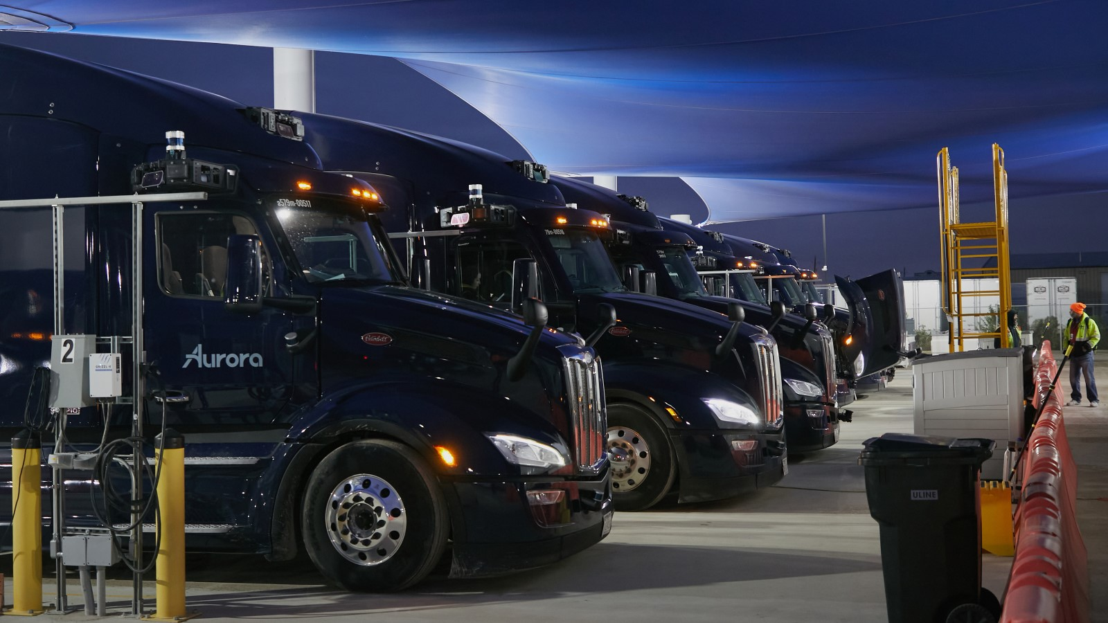 A photo of a fleet of self-driving trucks in a tent. 