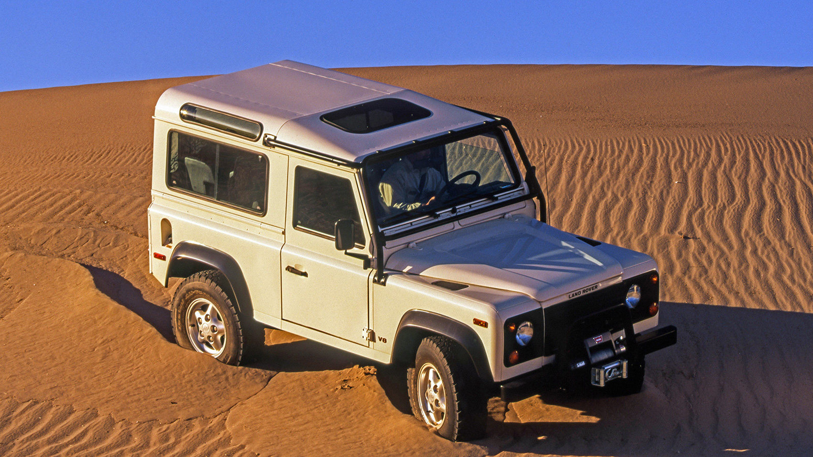 White Land Rover Defender front three-quarter angle view driving in desert