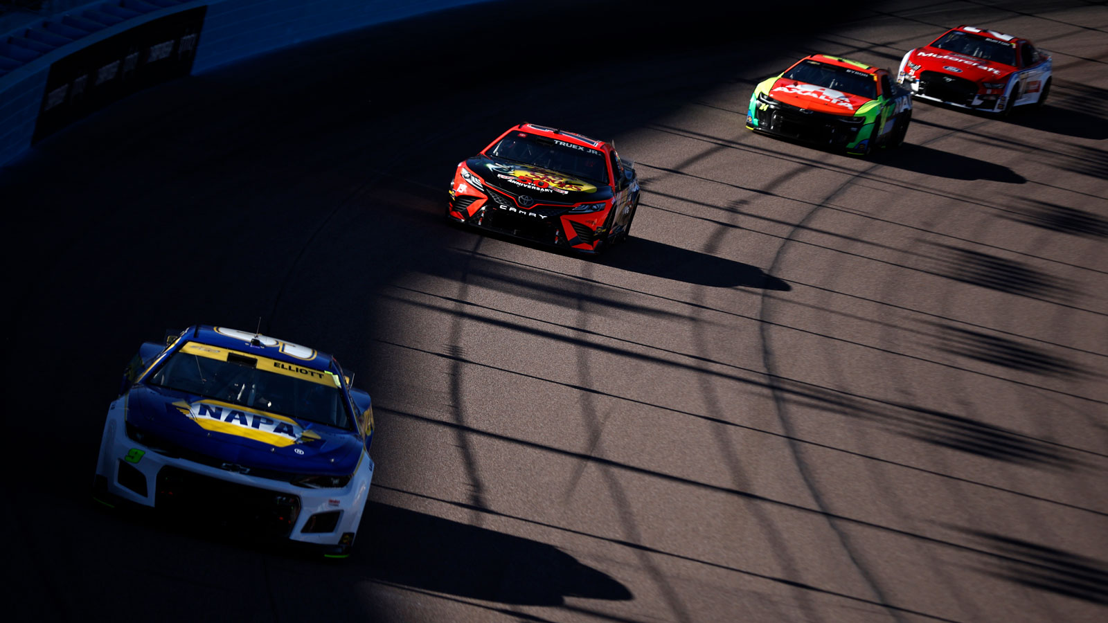 A photo of four Nascar racers driving round an oval track. 