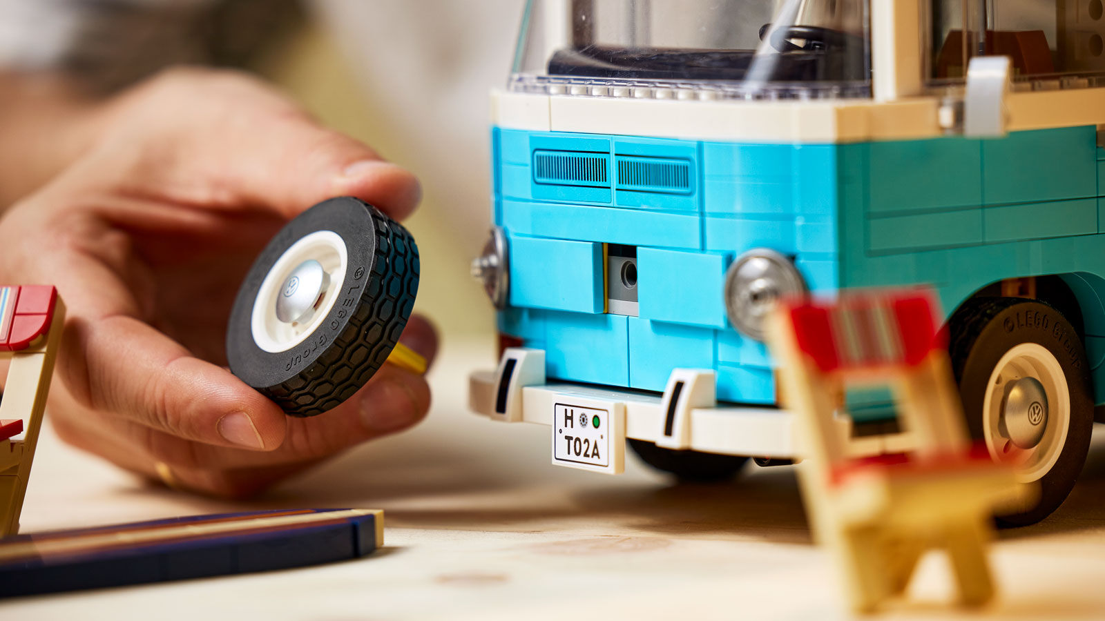 A photo of a Lego tire being fitted to a model VW bus. 