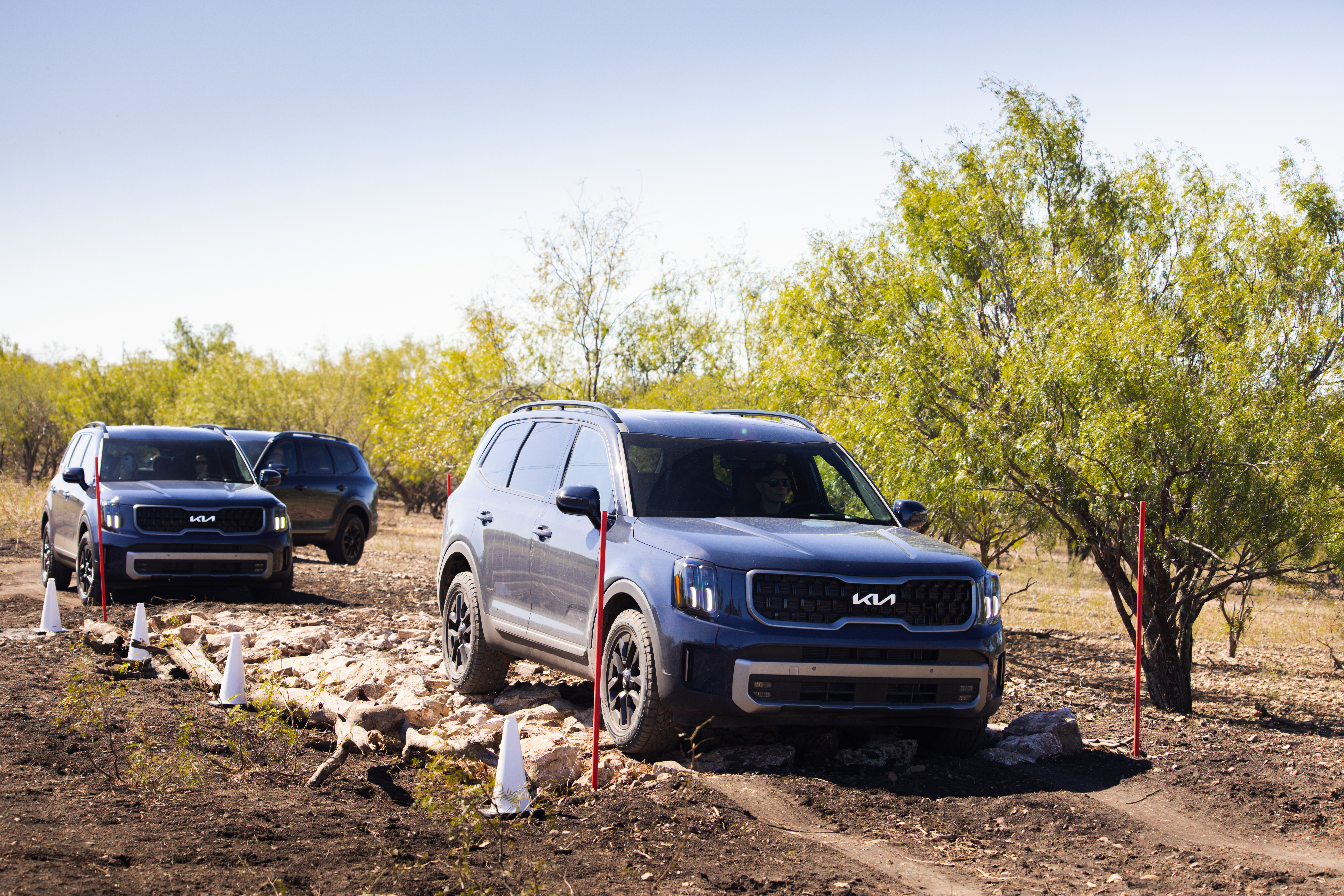 Three blue 2023 Kia Telluride SX X-Pro vehicles drive in a line on a dirt path in San Antonio, TX.