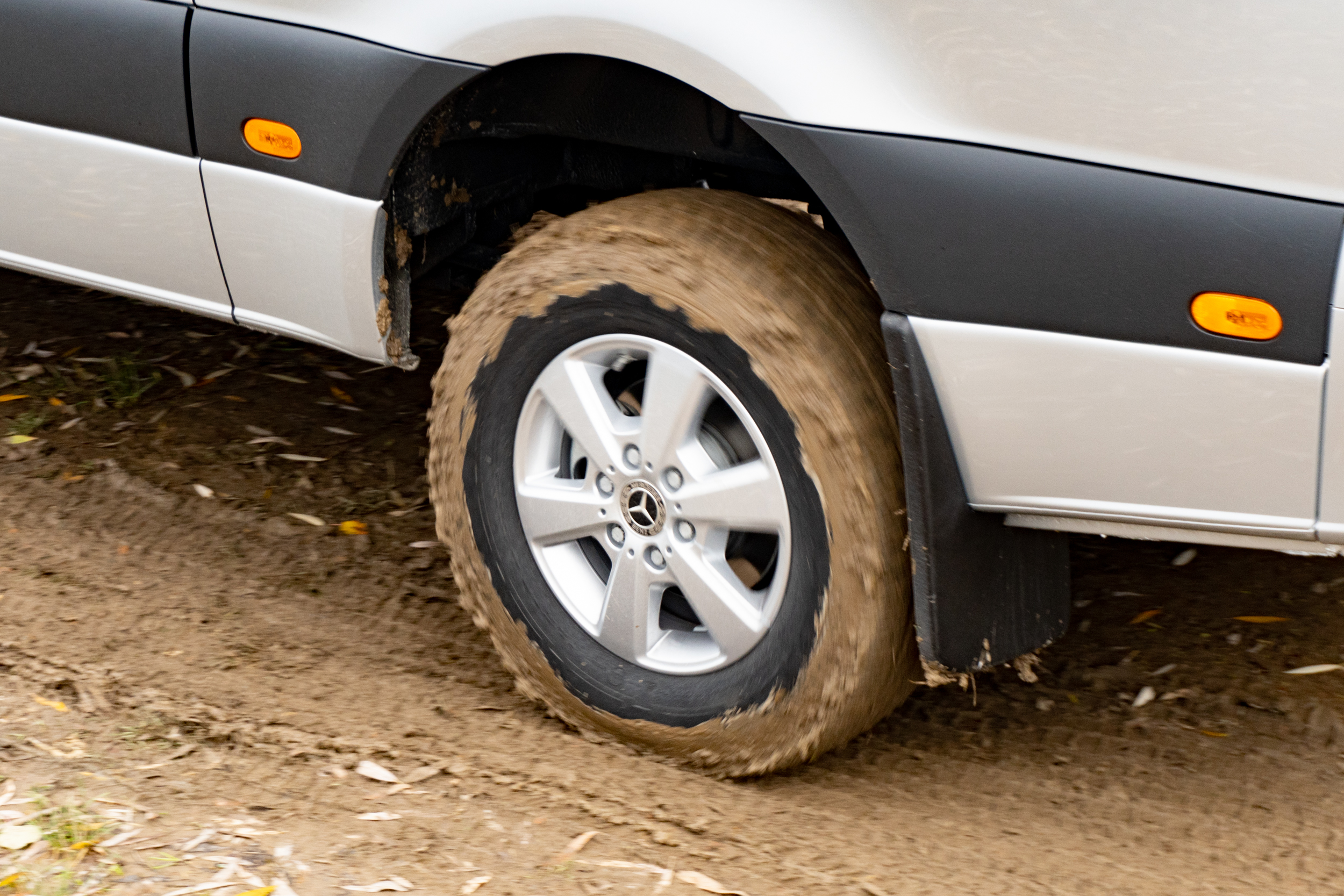 a close-up photo of the left rear wheel of a 2023 mercedes benz sprinter awd van. the van is driving on a muddy trail; the tire is completely caked in mud.