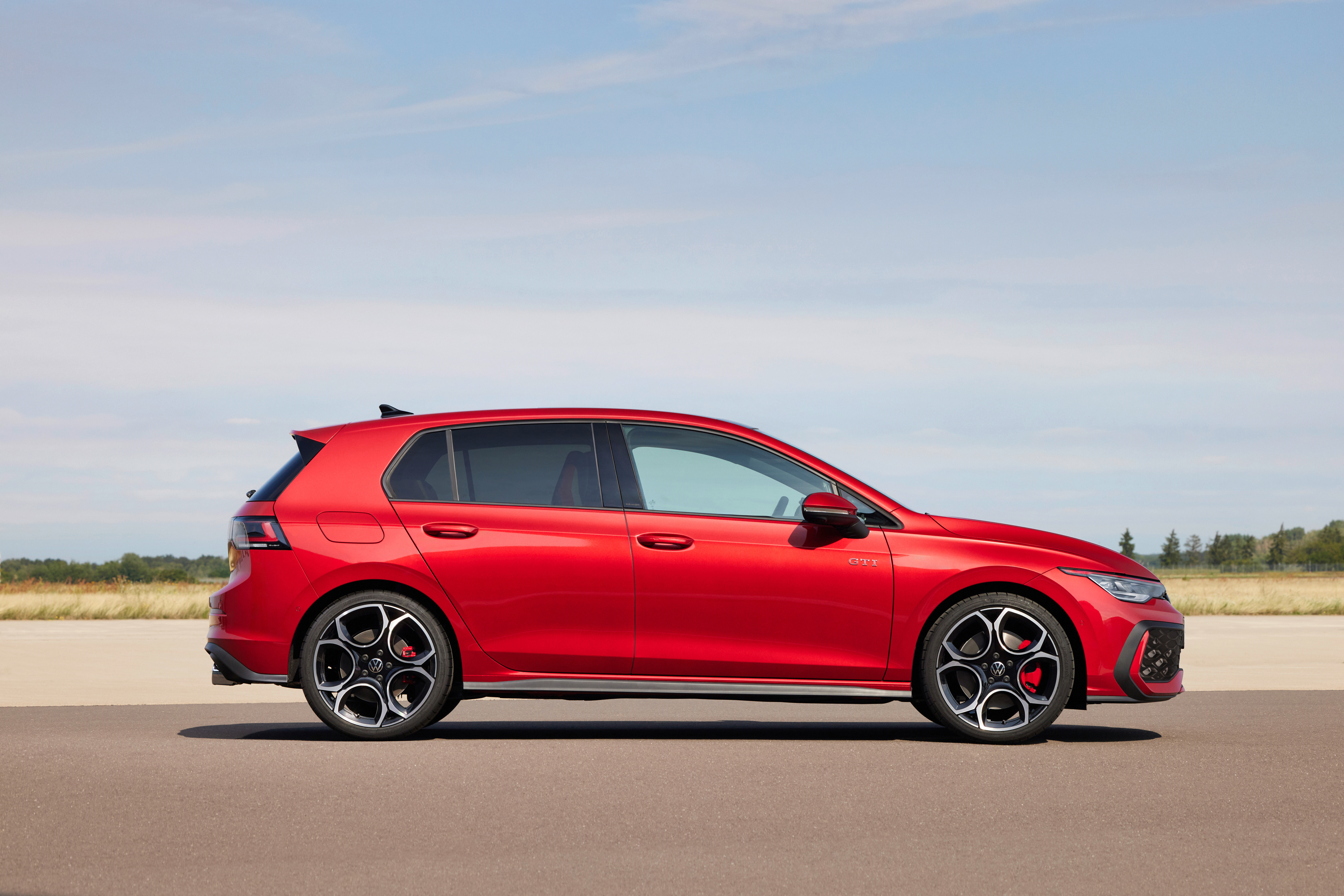 A side view of the new GTI in bright red near a field 