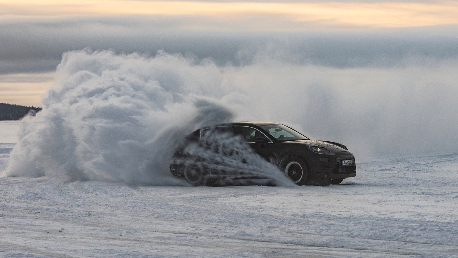 A photo of an electric Porsche Macan SUV driving on snow. 