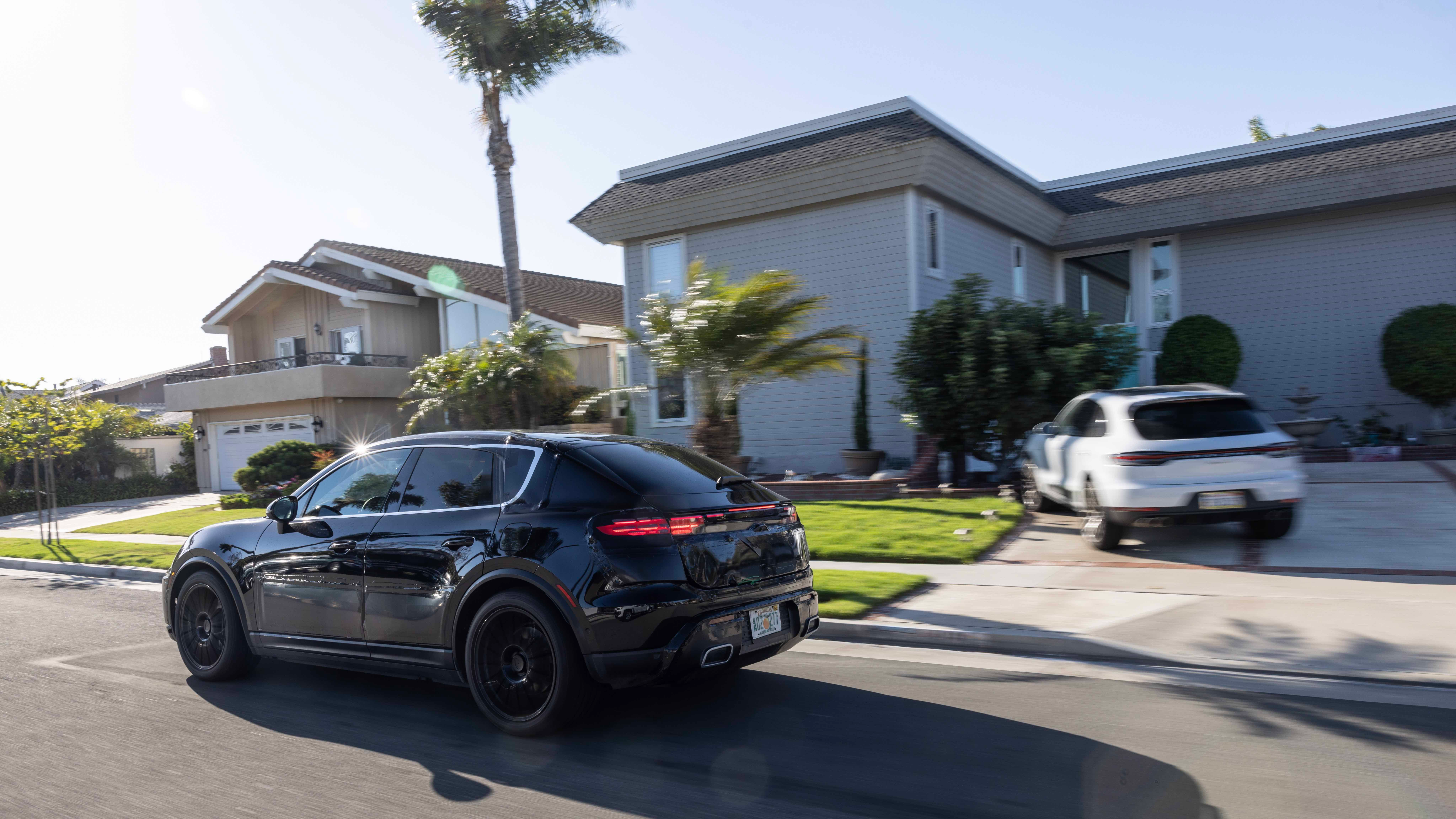 Rear 3/4 view of a camouflaged black Porsche Macan EV driving down a residential street