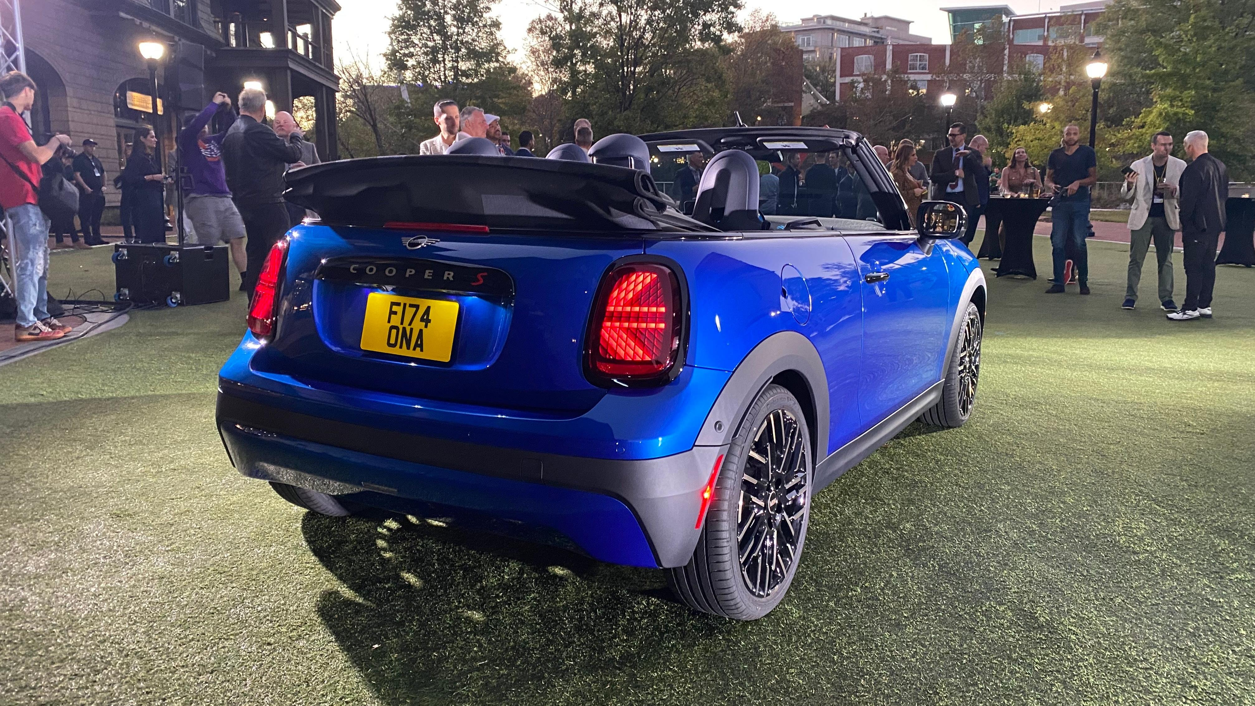 A rear three quarters photo of a bright blue Mini Cooper S Convertible parked on grass